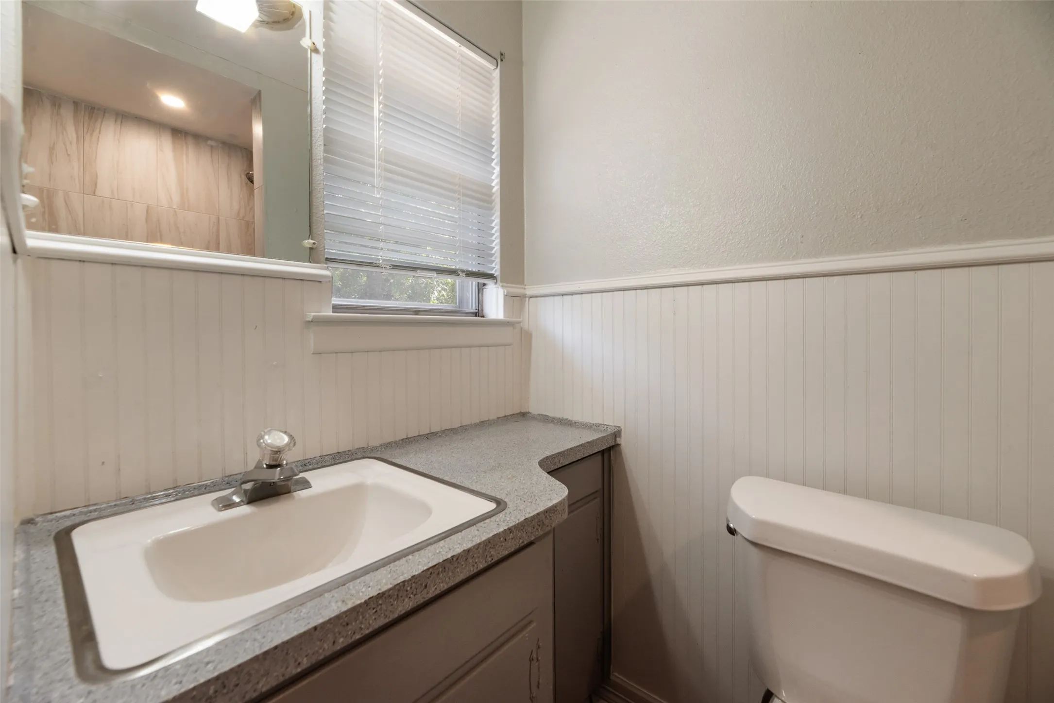 Bathroom featuring a built-in vanity with an integrated sink, a large mirror, and wainscoting