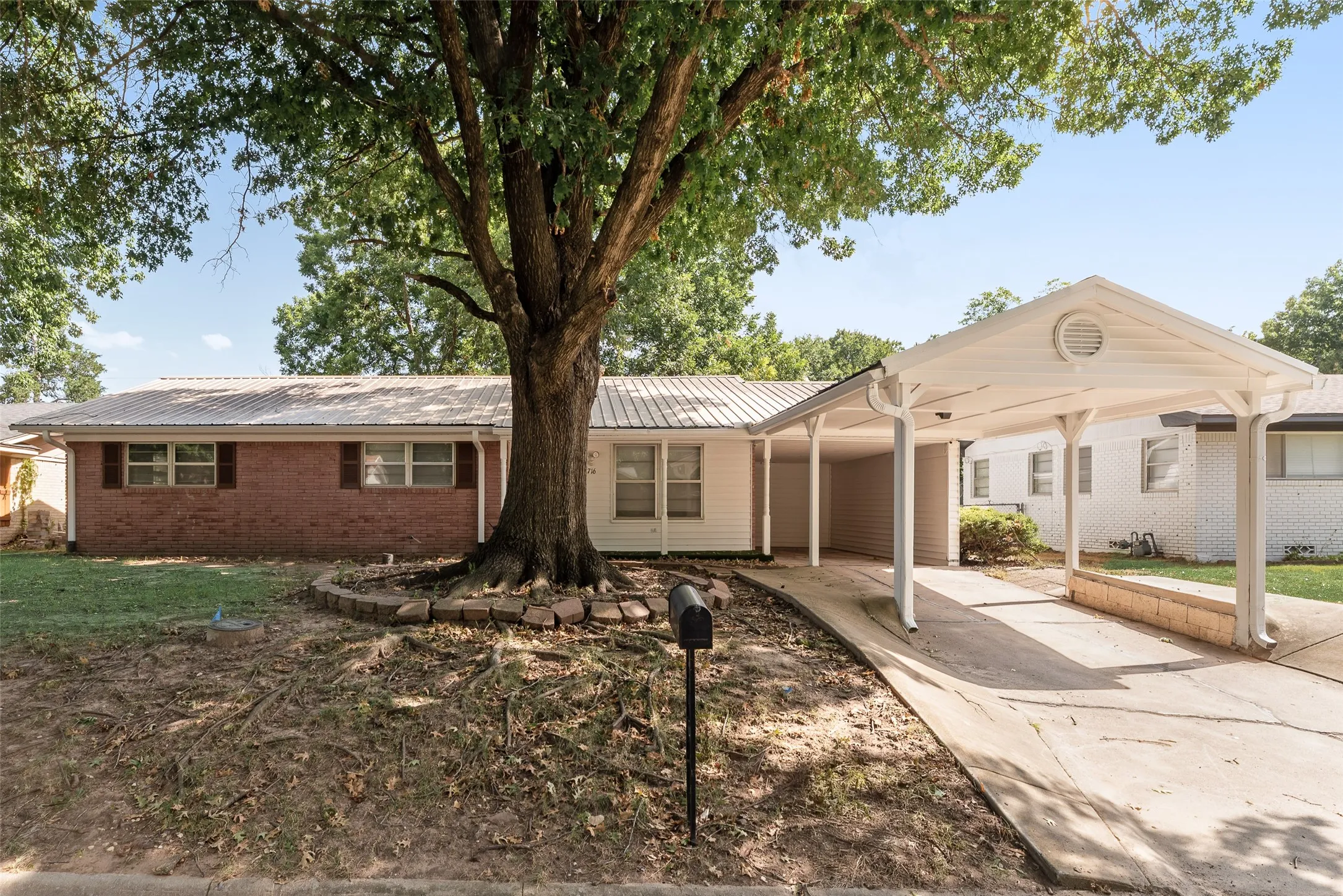 Brick and siding exterior with a metal roof, featuring a covered carport and mature trees