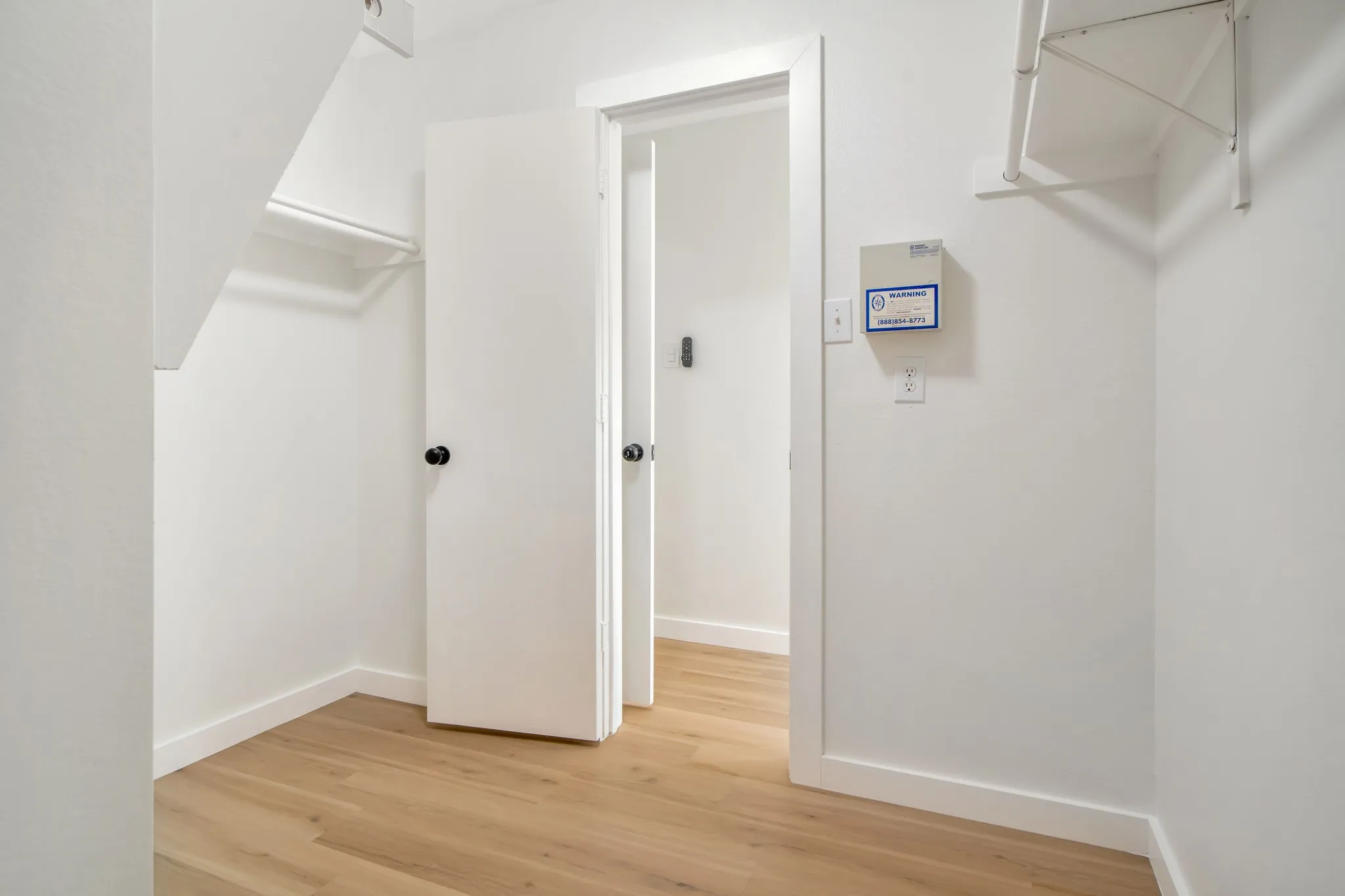 Wood-finish flooring throughout, bright white walls, and a window with horizontal blinds