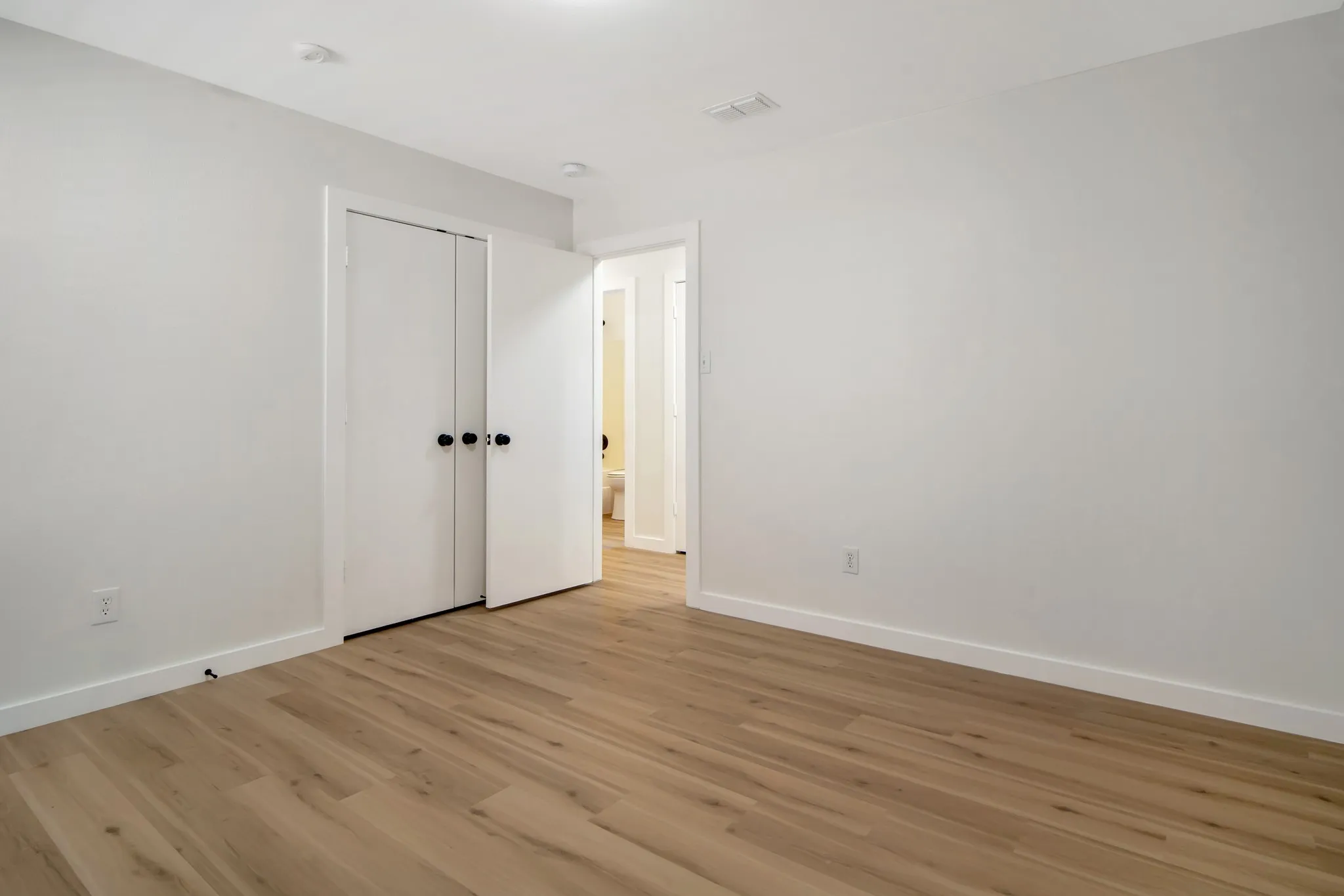Utility area featuring wood-finish flooring, a white shelving unit, and a white entry door with matte black hardware