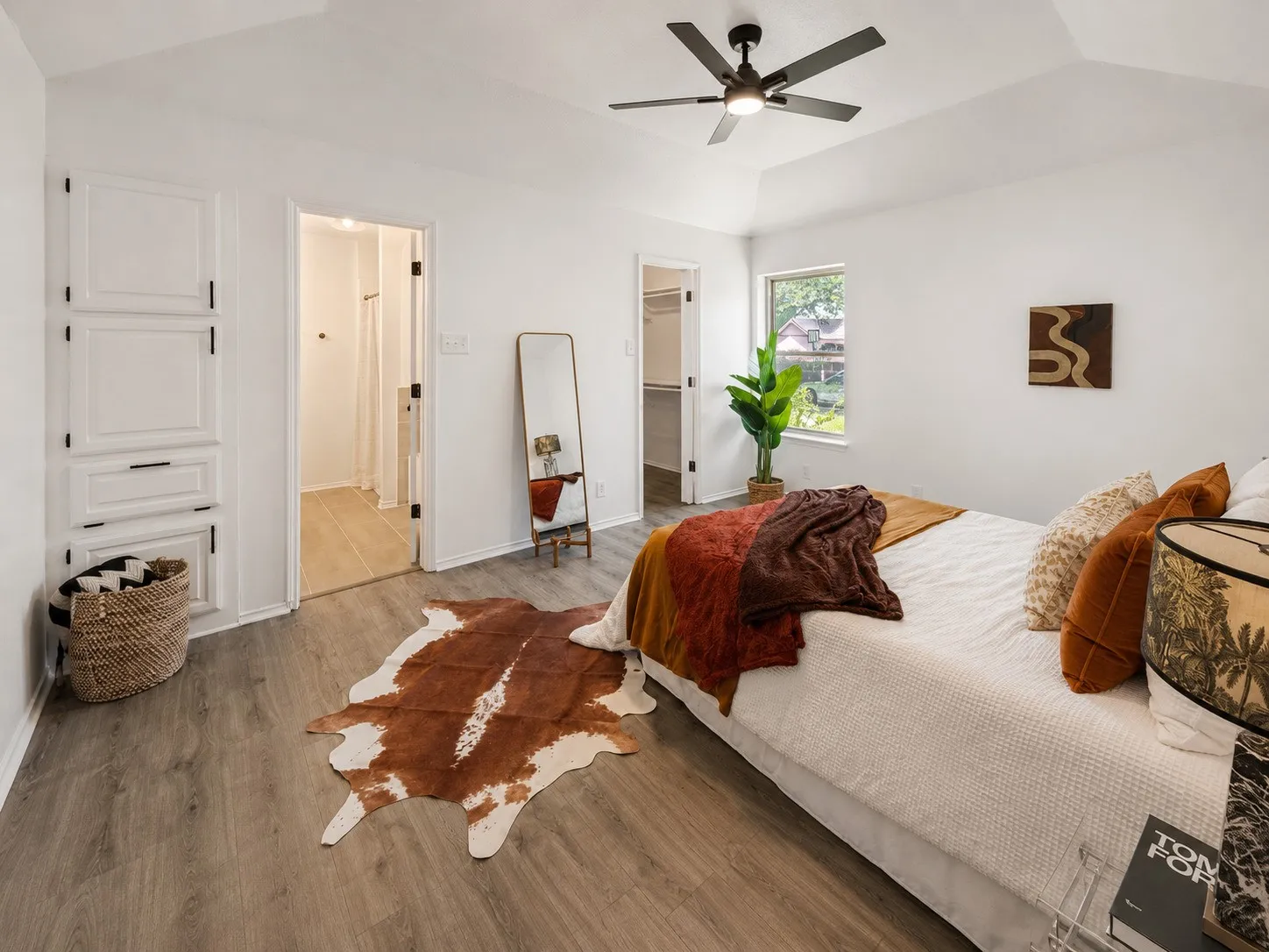 Vaulted ceiling with a ceiling fan, wood-finish flooring, built-in white cabinetry with dark hardware, and a window providing natural light