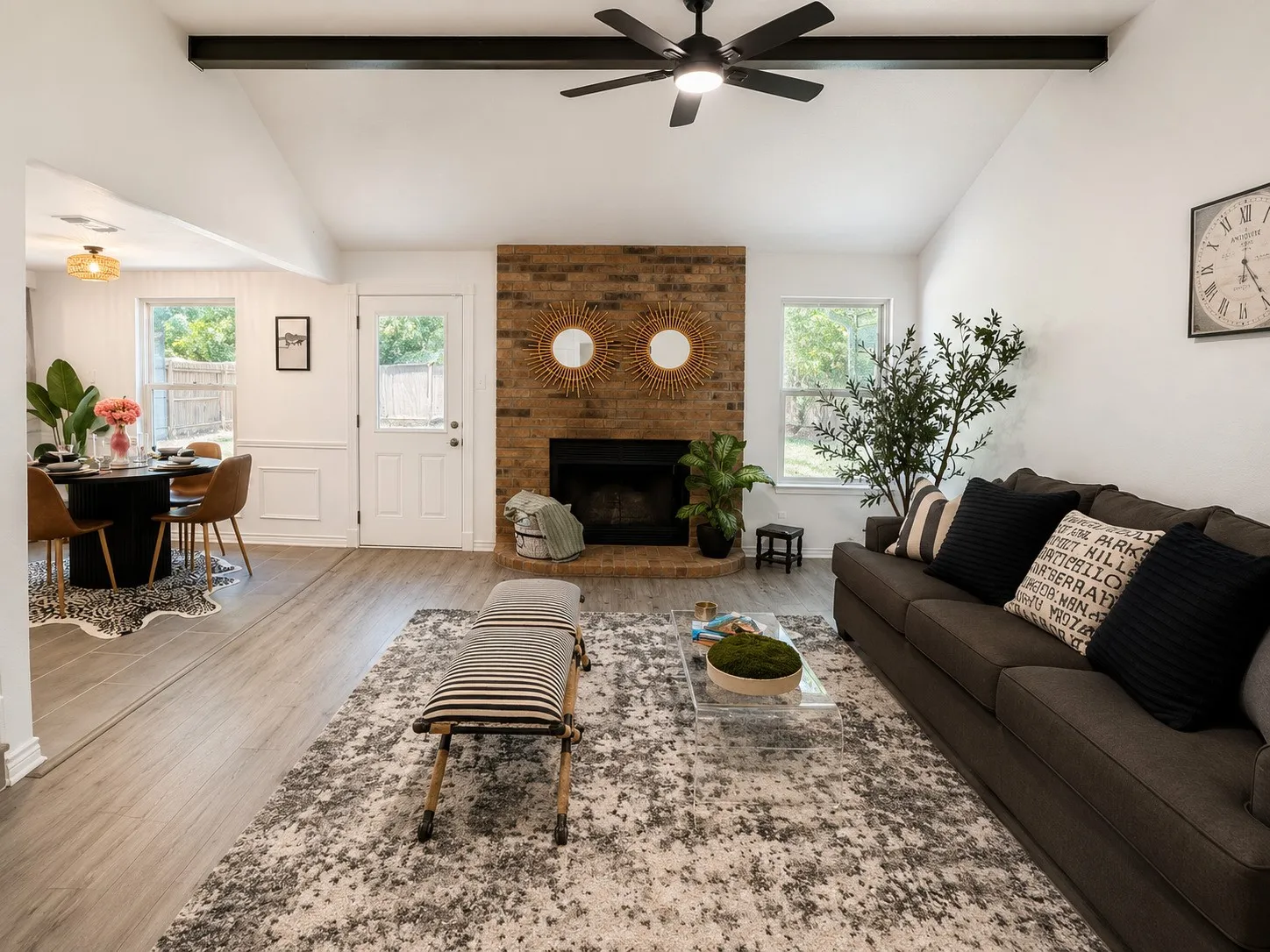 Vaulted ceilings with exposed beams, brick fireplace, wood-finish flooring, and a ceiling fan