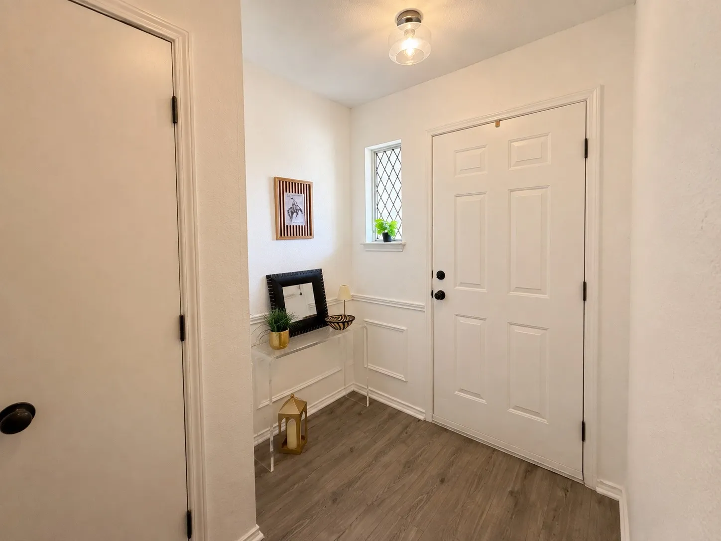 Wood-finish flooring, paneled entry door with black hardware, decorative window with lattice, wainscoting, and flush mount lighting