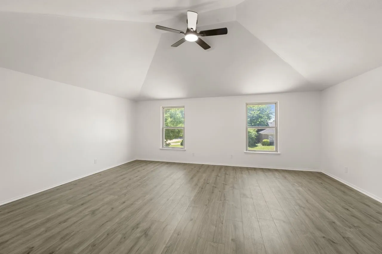Vaulted ceiling with a ceiling fan, two windows, and wood-finish flooring