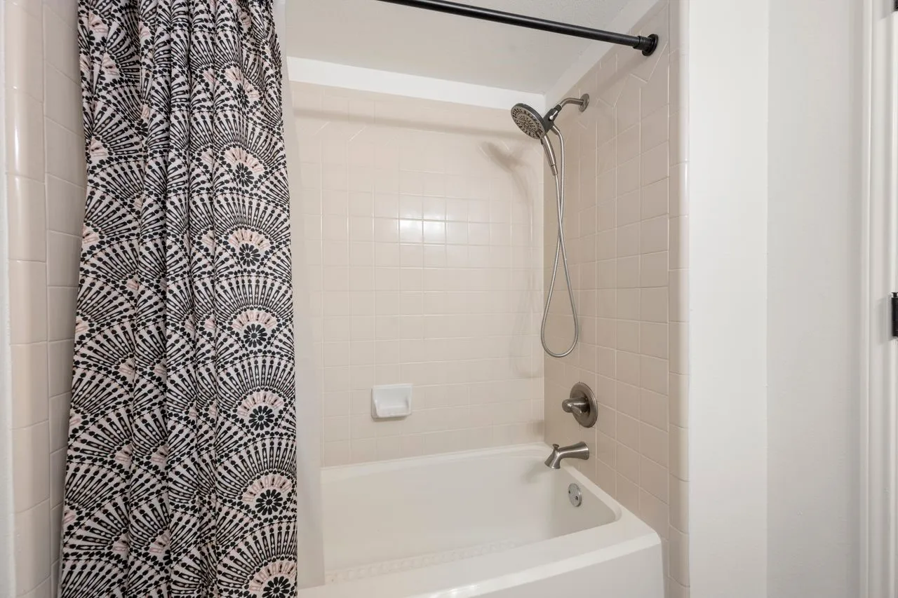 Bathtub with tiled surround, brushed nickel fixtures, and a multi-function showerhead