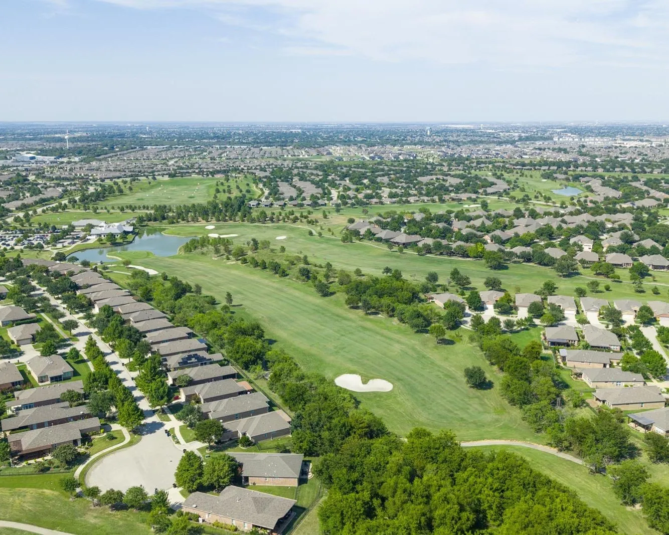 Aerial overview of a residential area with a golf course, expansive green spaces, and a body of water