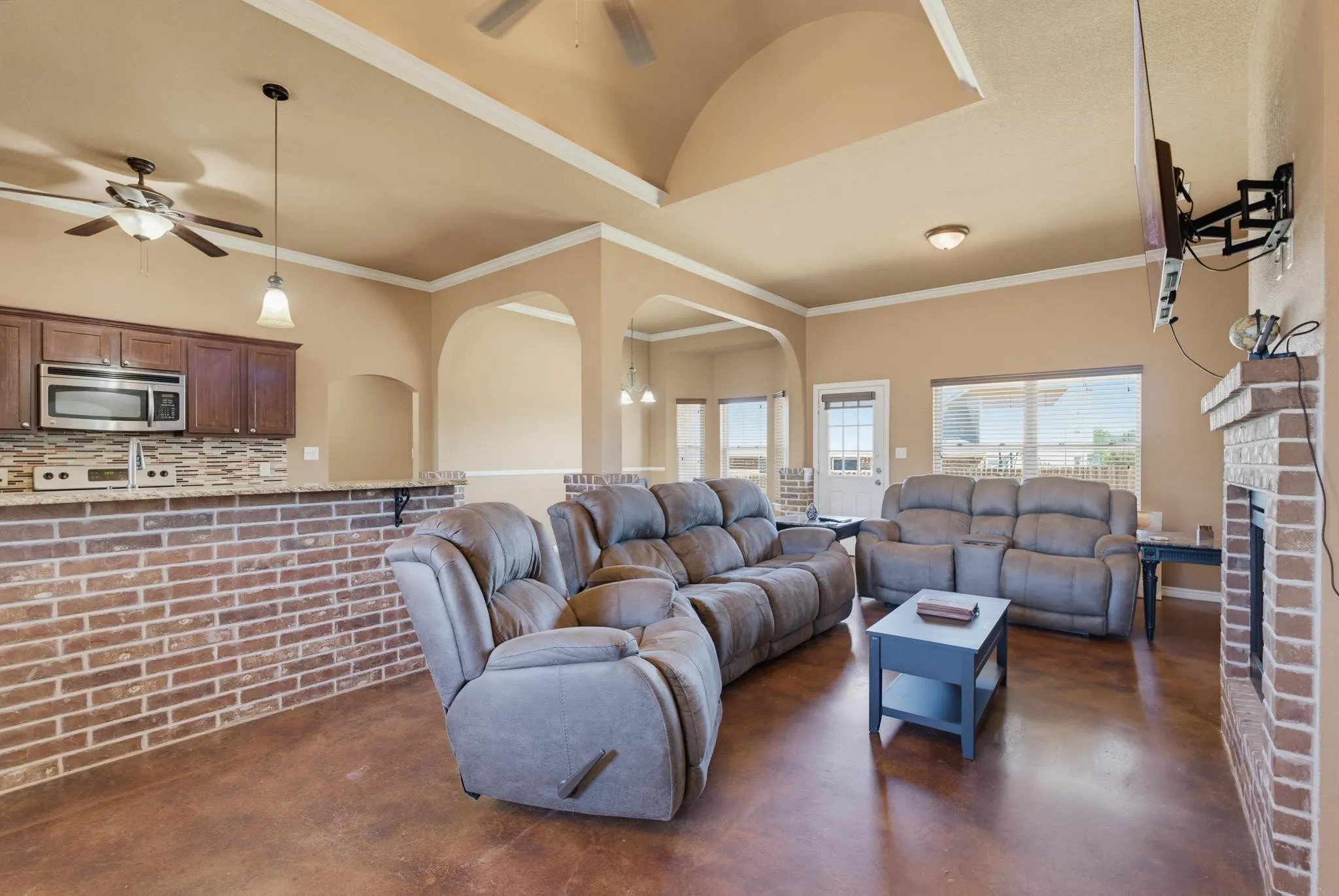 Arched doorways, brick accent wall, brick fireplace, vaulted ceiling, and wood-finish flooring
