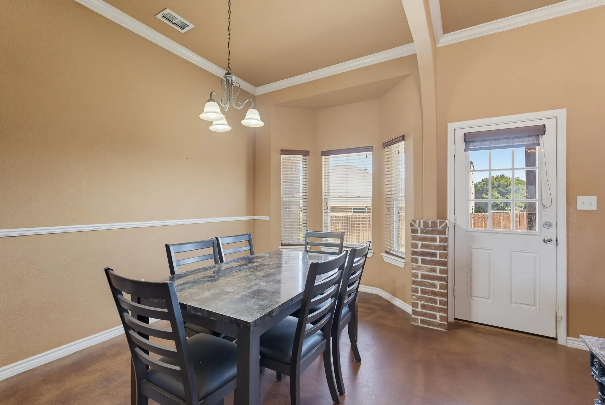 Tray ceiling with decorative crown molding, pendant light fixture, bay window, and a door with an integrated window grid