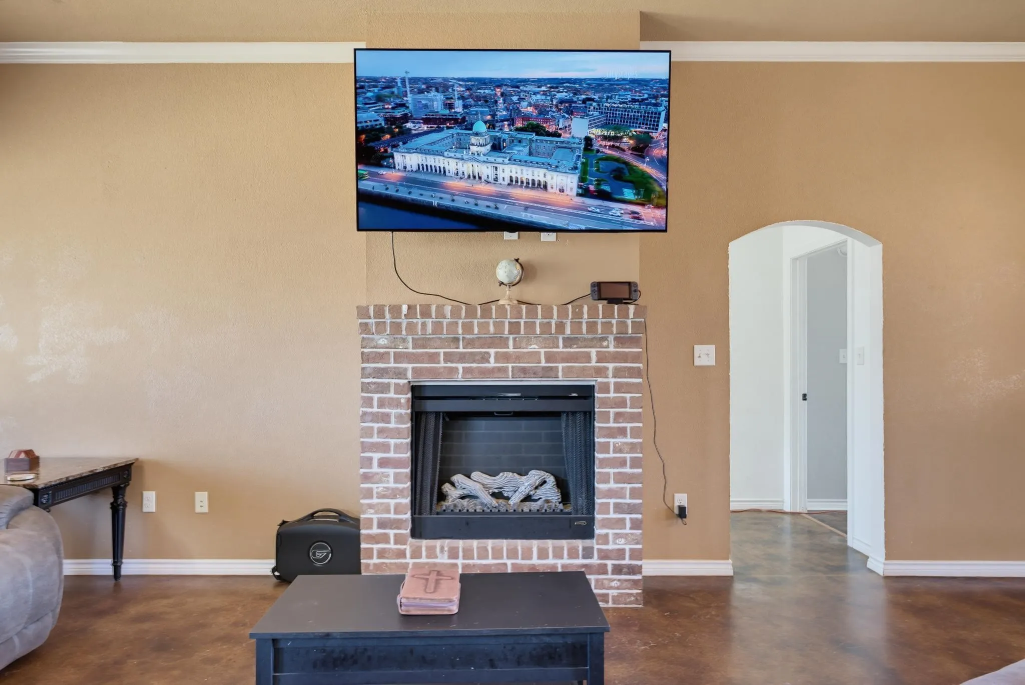 Brick fireplace with a black firebox and mantle, complementing wood-finish flooring, and white crown molding