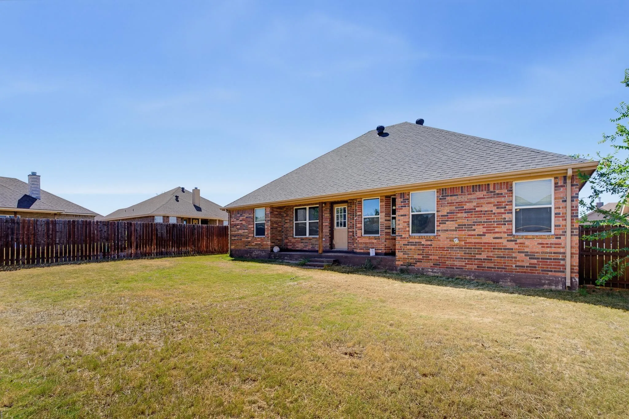 Expansive backyard featuring a wood fence, brick exterior, and a covered patio area