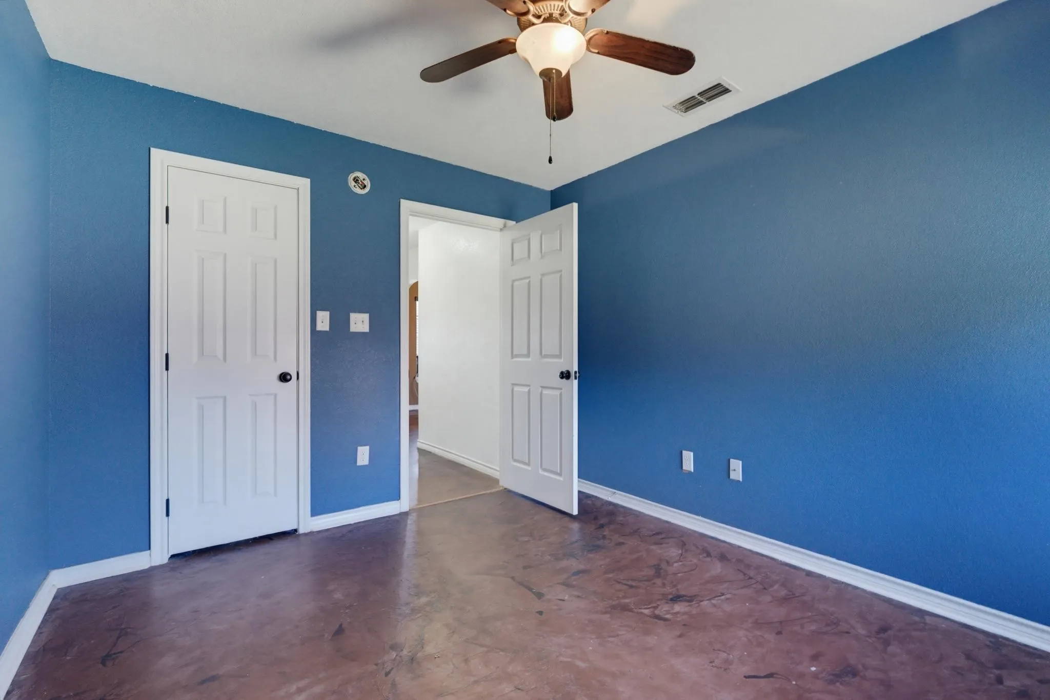 Stained concrete flooring, blue wall finish, white trim, white interior doors, and a ceiling fan