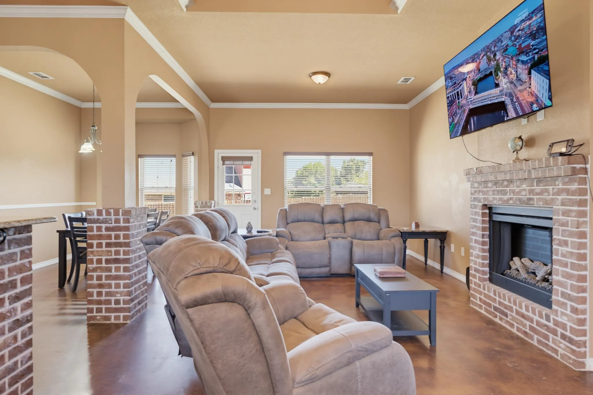 Brick fireplace with a gas log insert, crown molding, arched doorways, tray ceiling, and wood-finish flooring