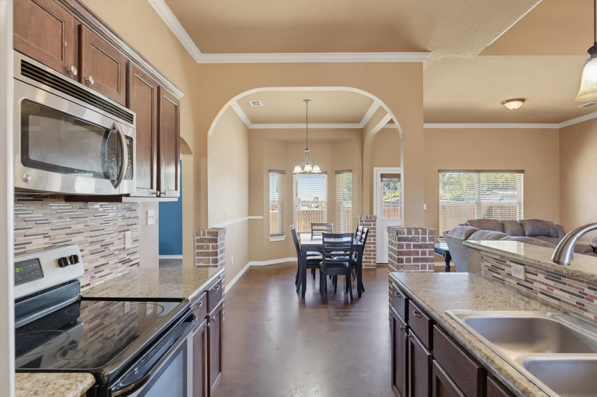 Stainless steel microwave, integrated electric cooktop, granite-style countertops, wood-finish cabinetry, and decorative tile backsplash