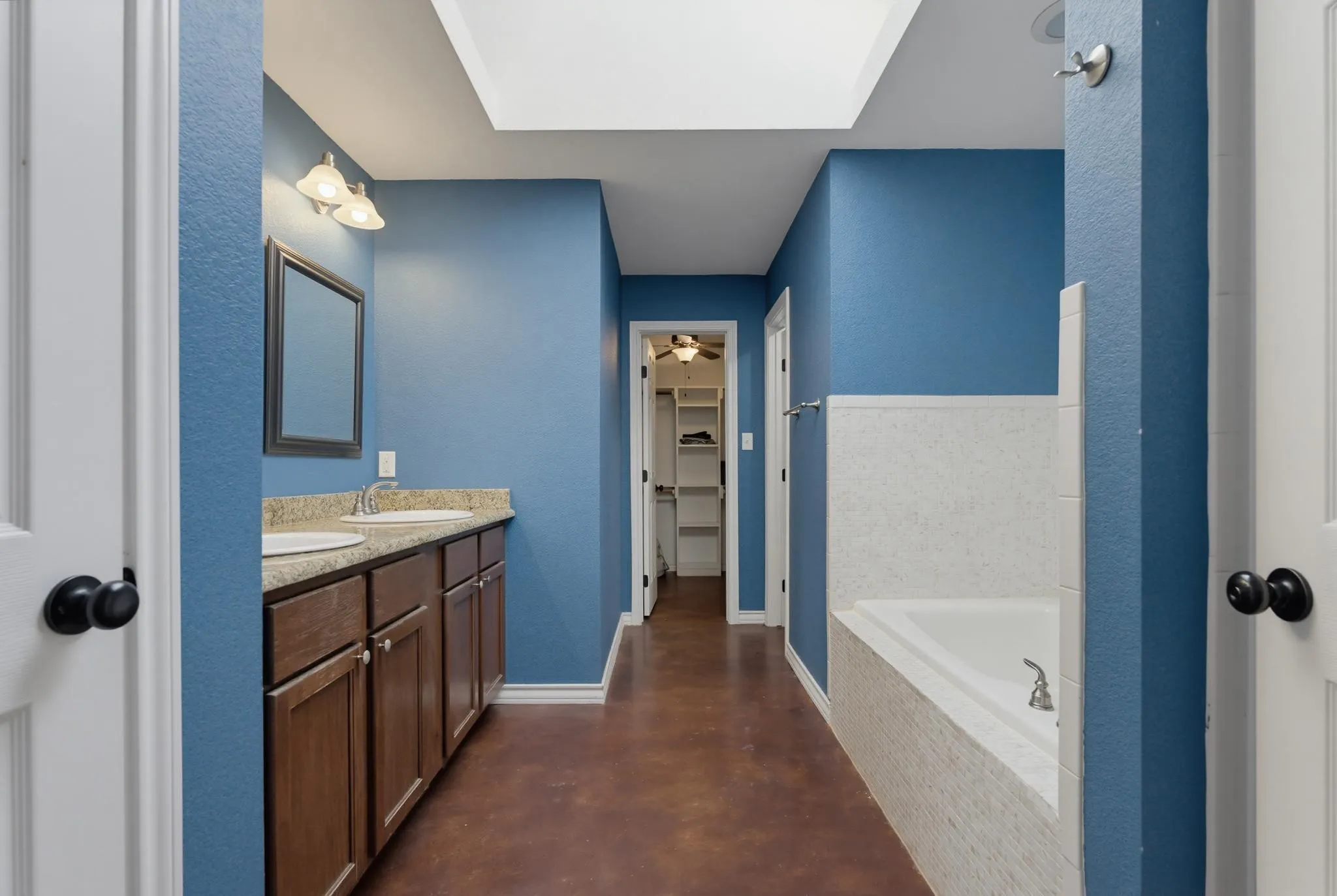 Dual vanity with undermount sinks, built-in bathtub with tiled surround, skylight, and wood-finish flooring