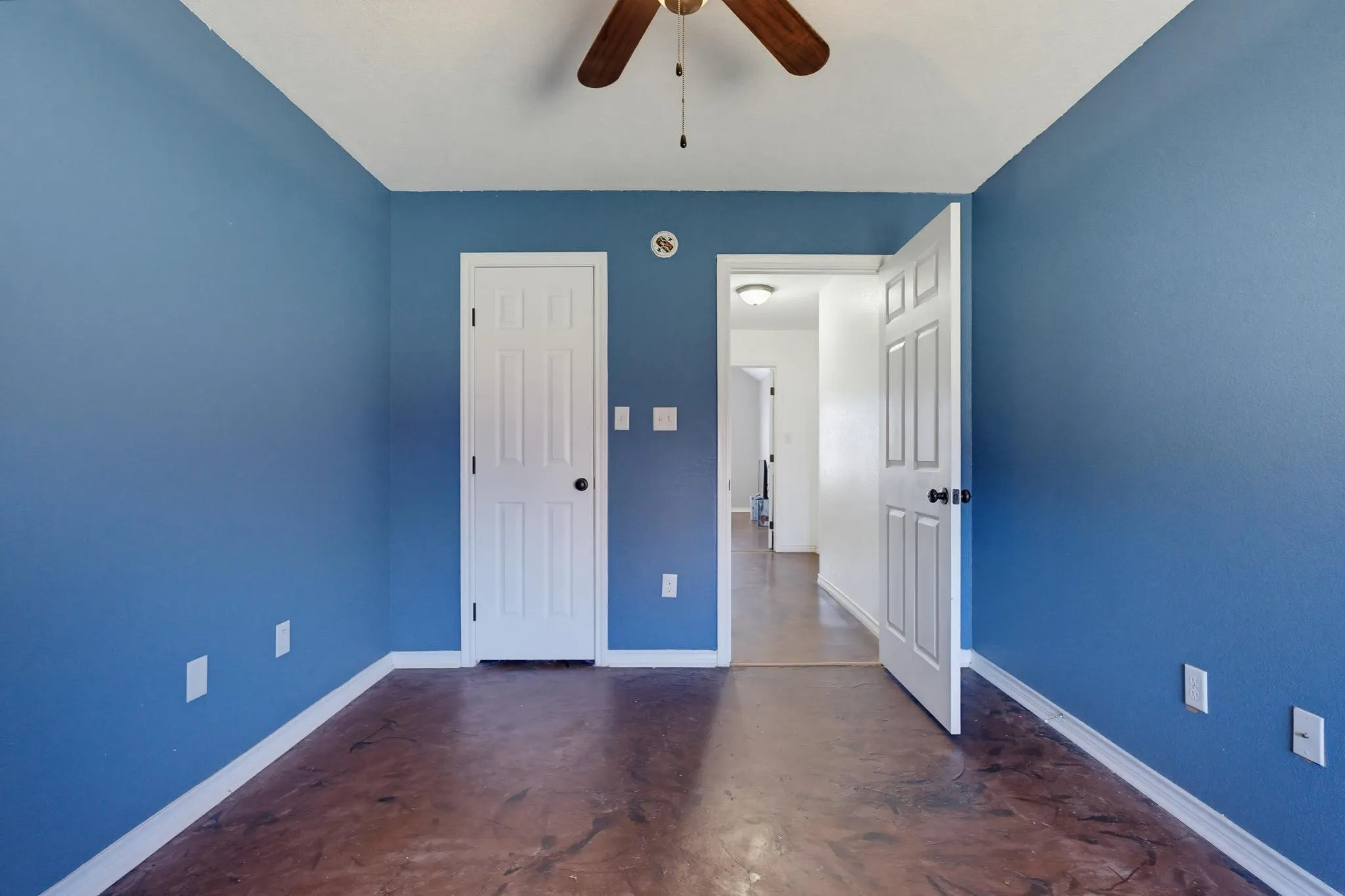 Textured blue walls with white trim, wood-finish flooring, and a ceiling fan with integrated lighting