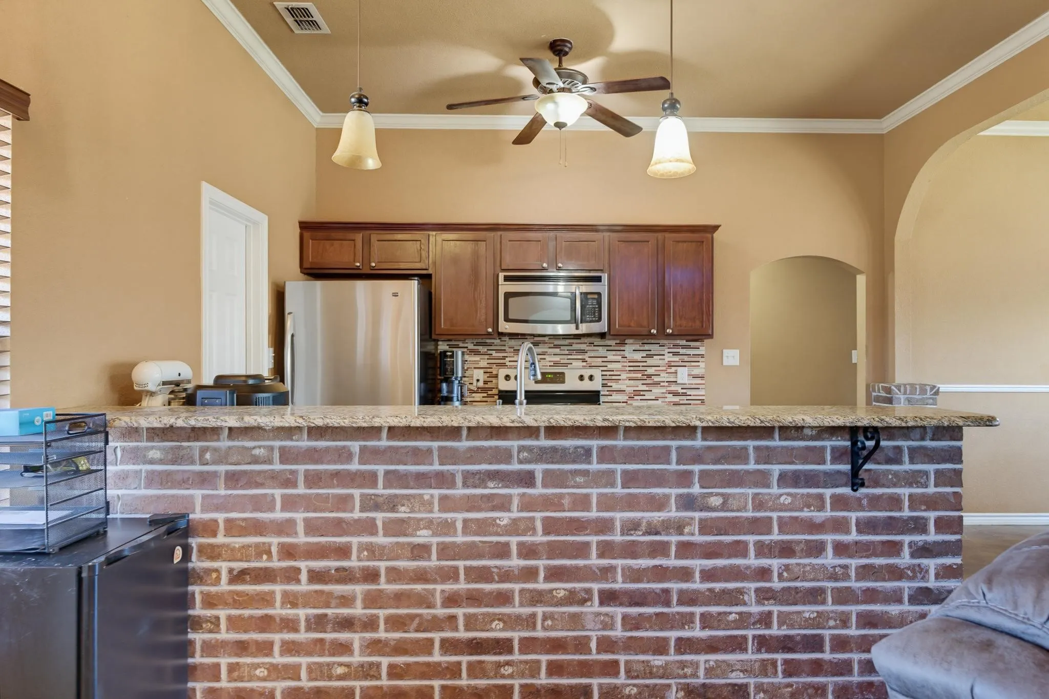 Brick-clad breakfast bar with a stone-finish countertop, stainless steel appliances, dark wood-finish cabinetry, and a mosaic tile backsplash