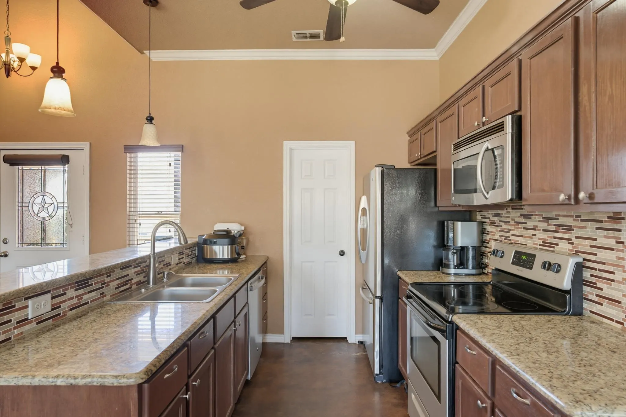 Kitchen featuring granite-style countertops, stainless steel appliances, a mosaic tile backsplash, and dark wood cabinetry