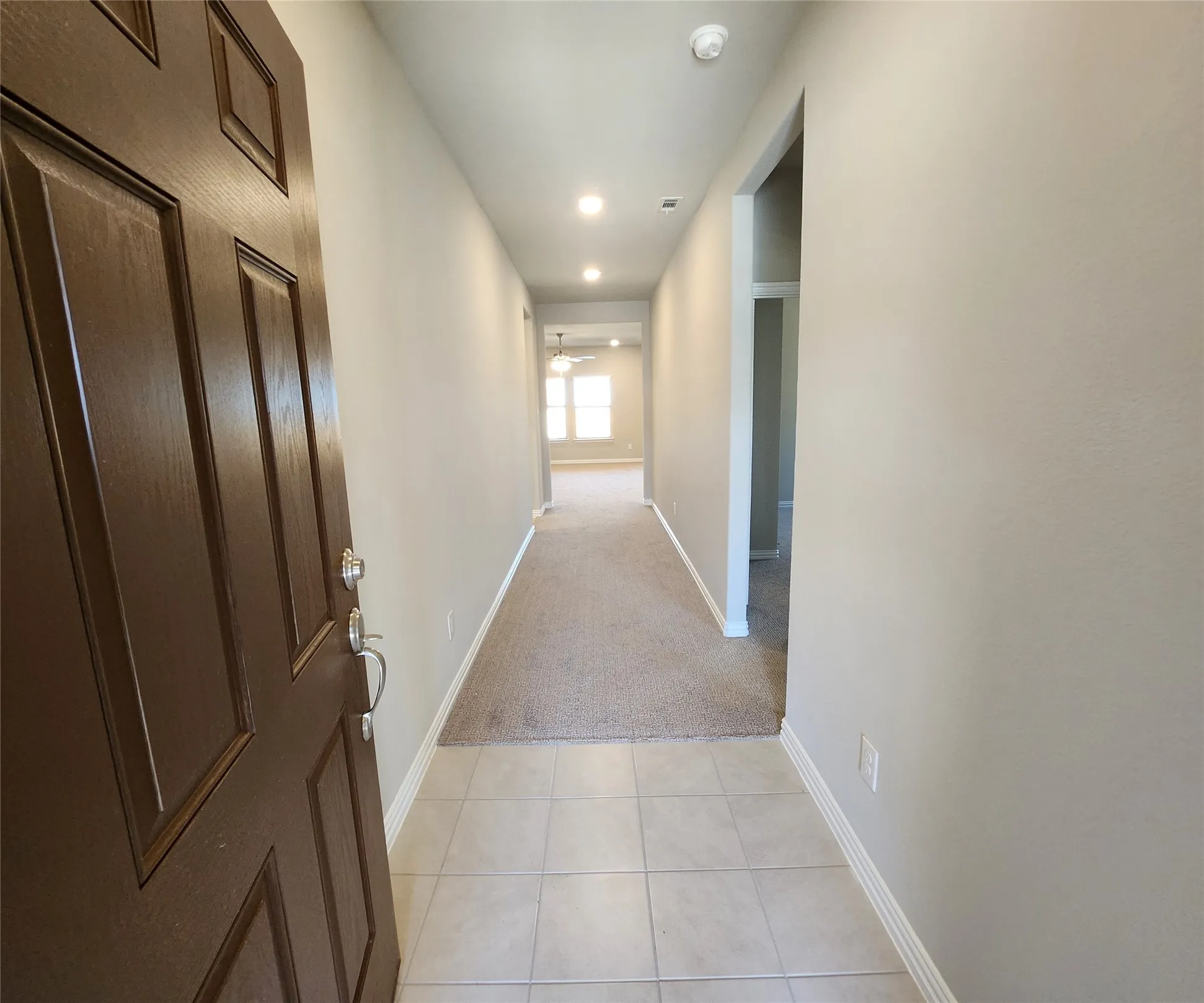 Entryway with tile flooring, leading to a carpeted hallway with recessed lighting