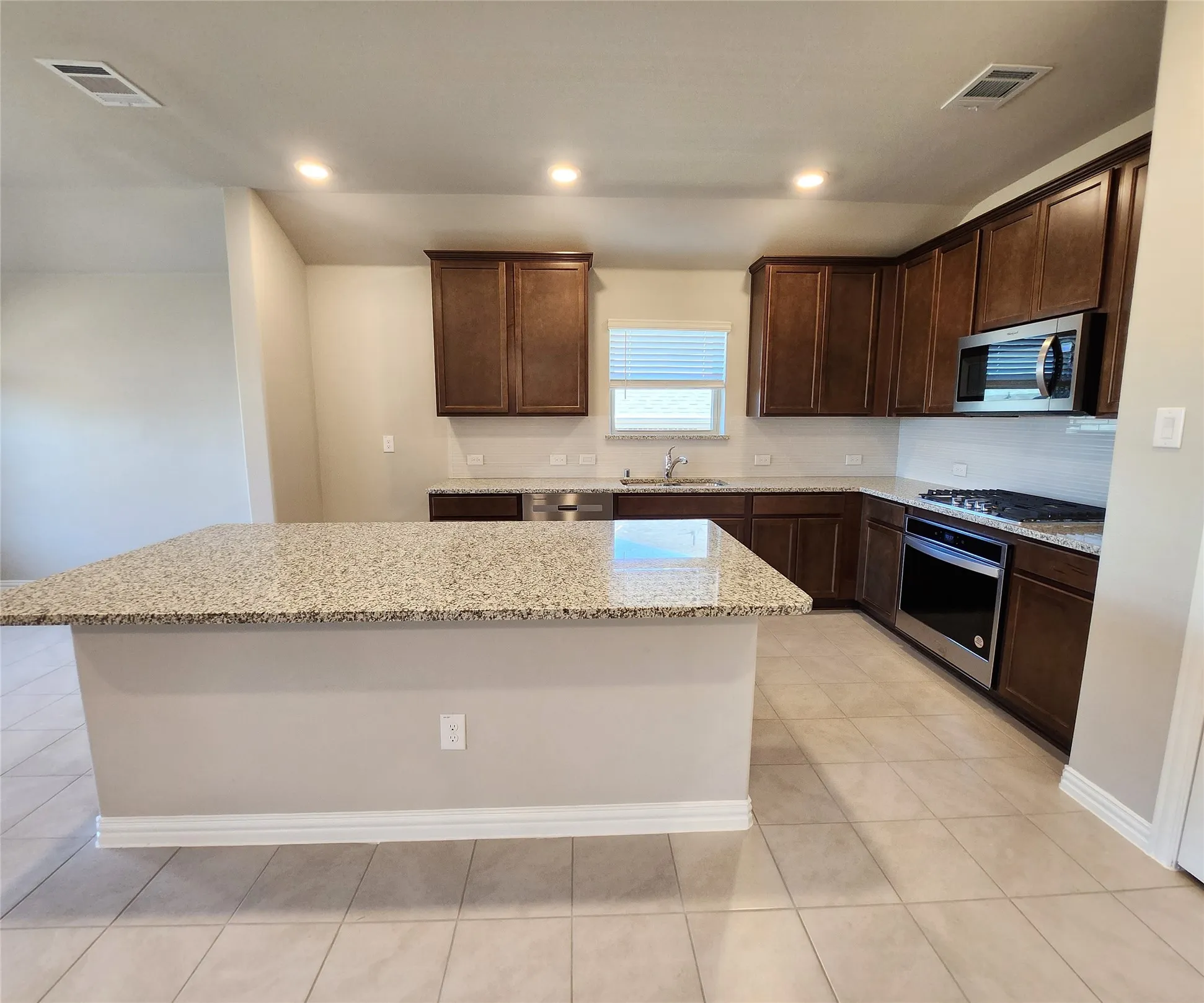 Kitchen featuring an island with stone countertops, dark wood-finish cabinetry, stainless steel appliances, and tile flooring