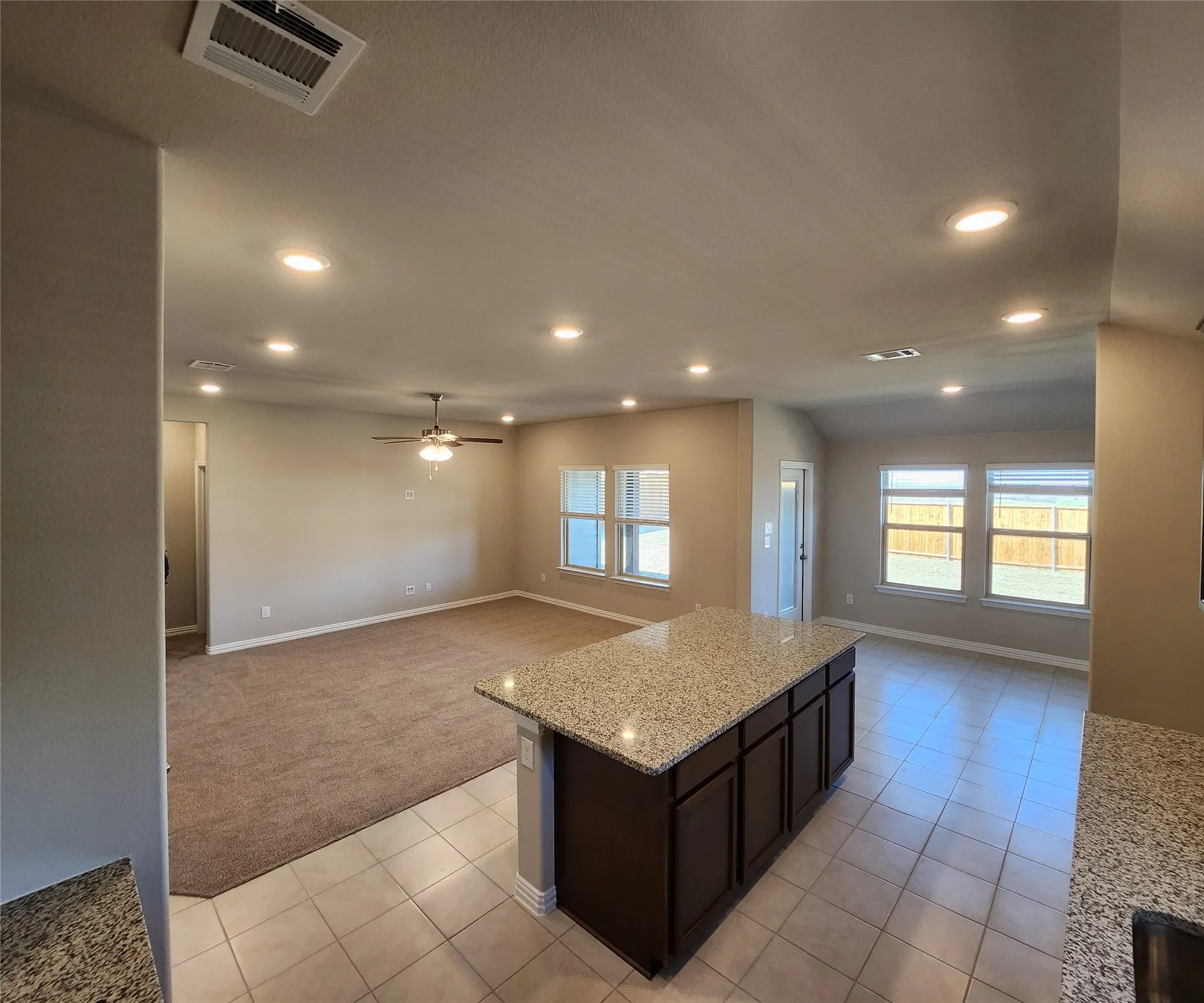 Open-concept living space featuring a central island with a granite countertop, recessed lighting, ceiling fan, and multiple windows