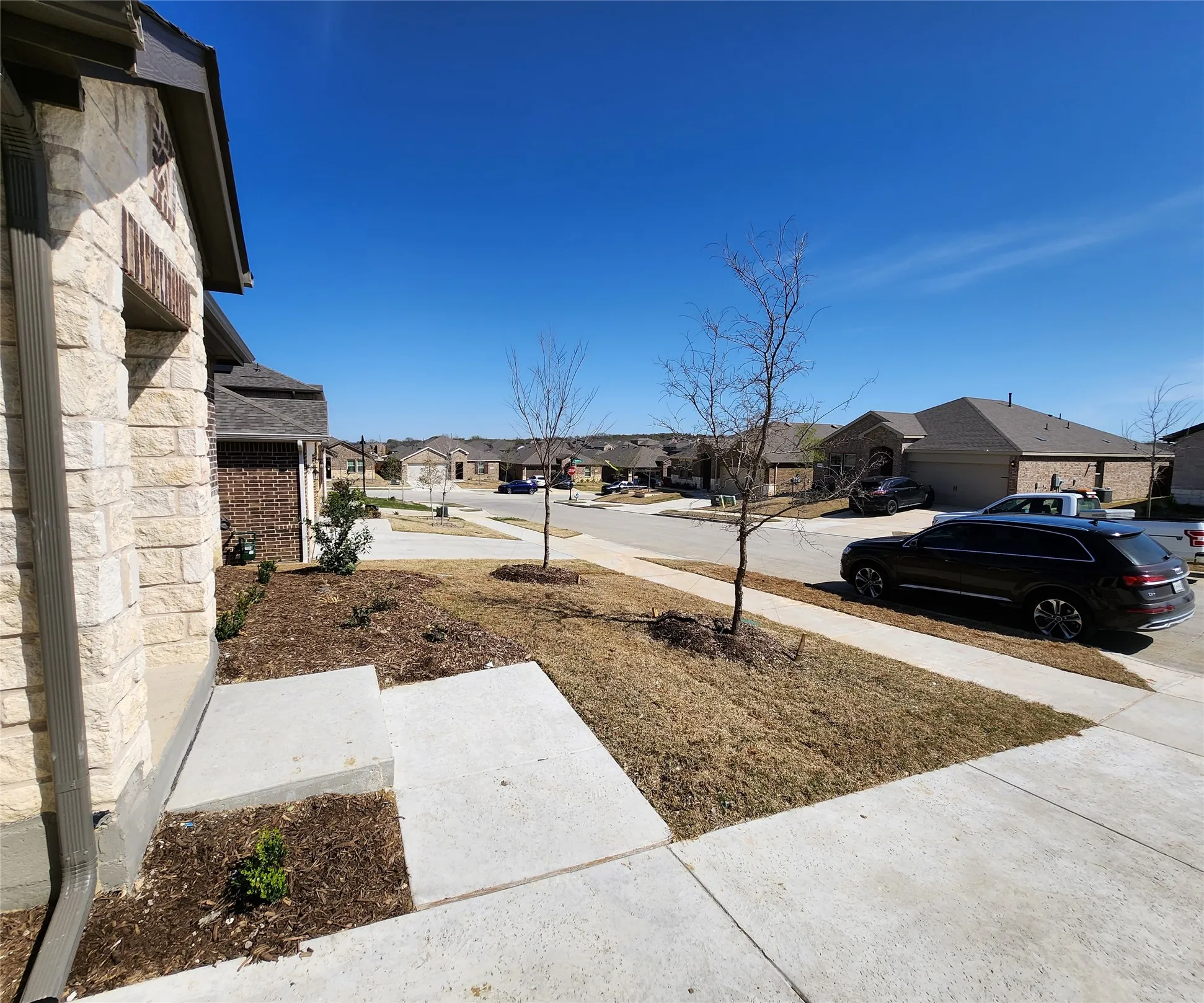 Stone and brick exterior facade with a dark shingle roof, concrete walkways, and landscape beds