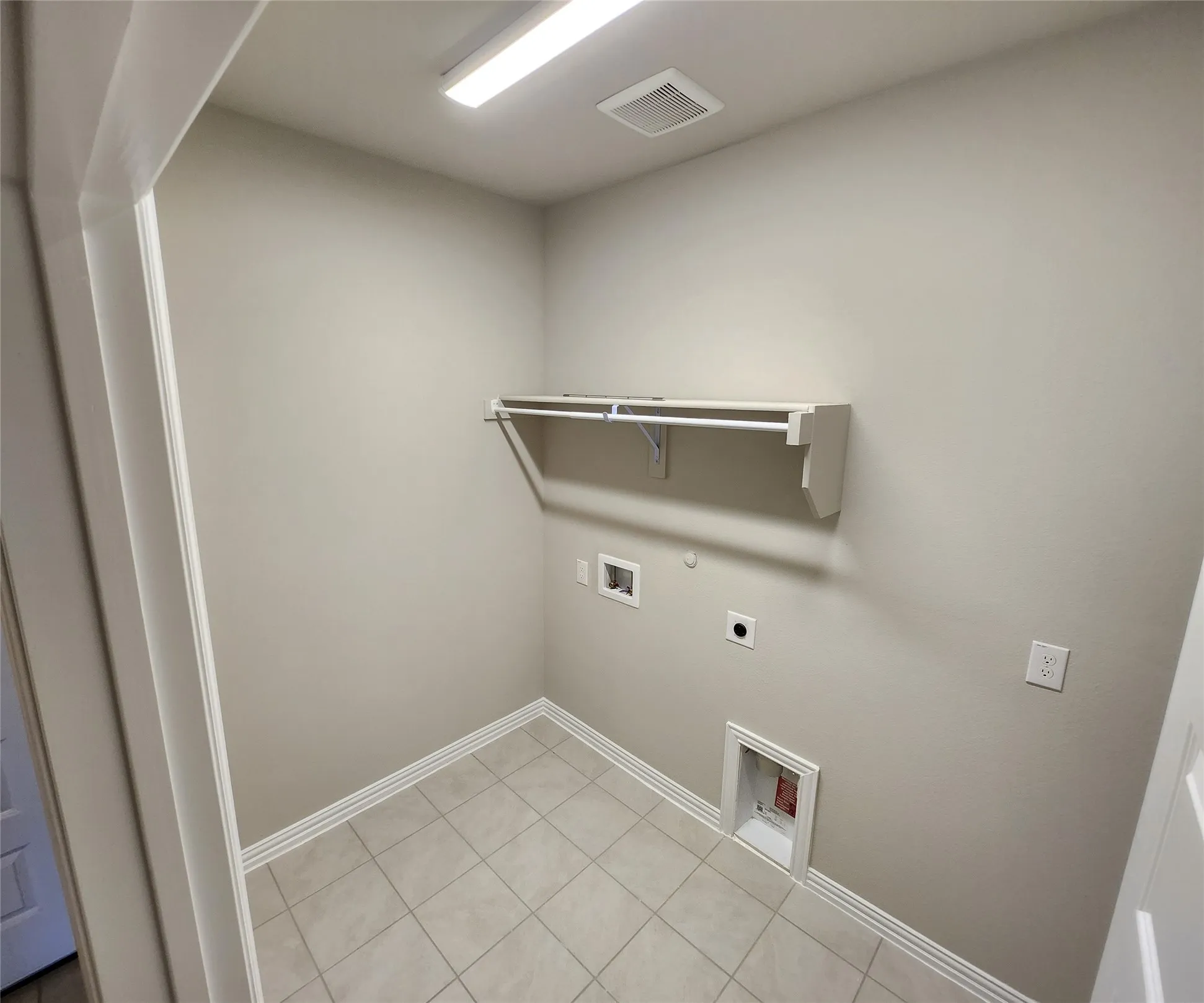 Dedicated laundry area featuring tile flooring, a built-in shelving unit with hanging rod, and utility hookups