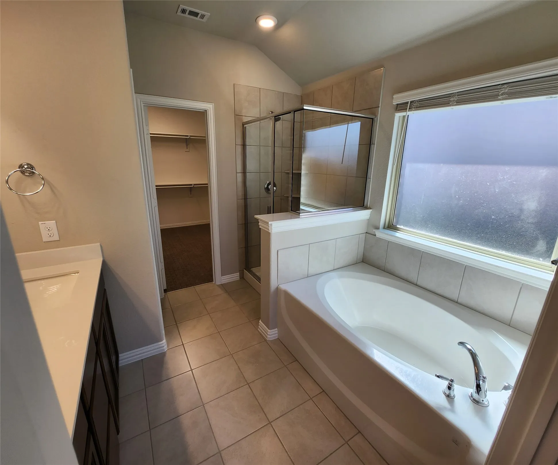 Soaking tub with tile surround, glass-enclosed shower, single vanity with sink, and tile flooring