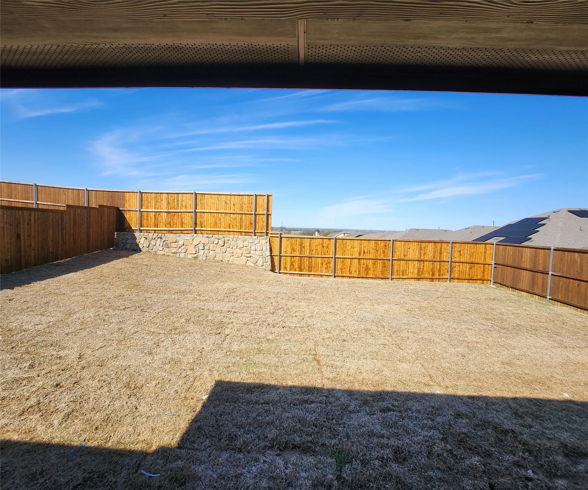 Expansive backyard featuring wood privacy fencing, a stone retaining wall, and a large grassy area