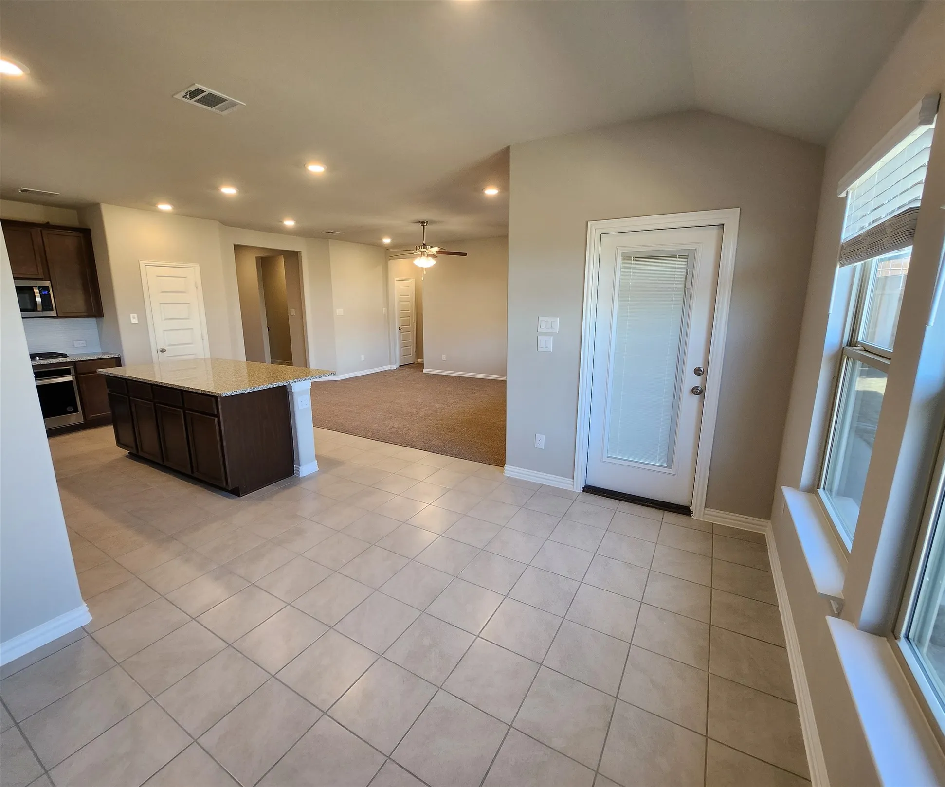 Open concept living space featuring a kitchen island with granite countertop, stainless steel appliances, tile flooring, and recessed lighting