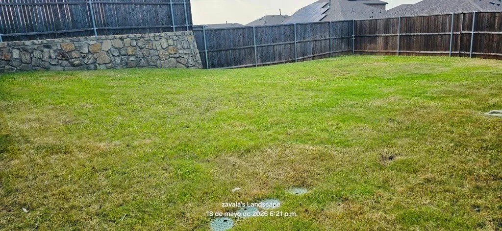 Expansive lawn area with a natural stone retaining wall and perimeter wood fencing