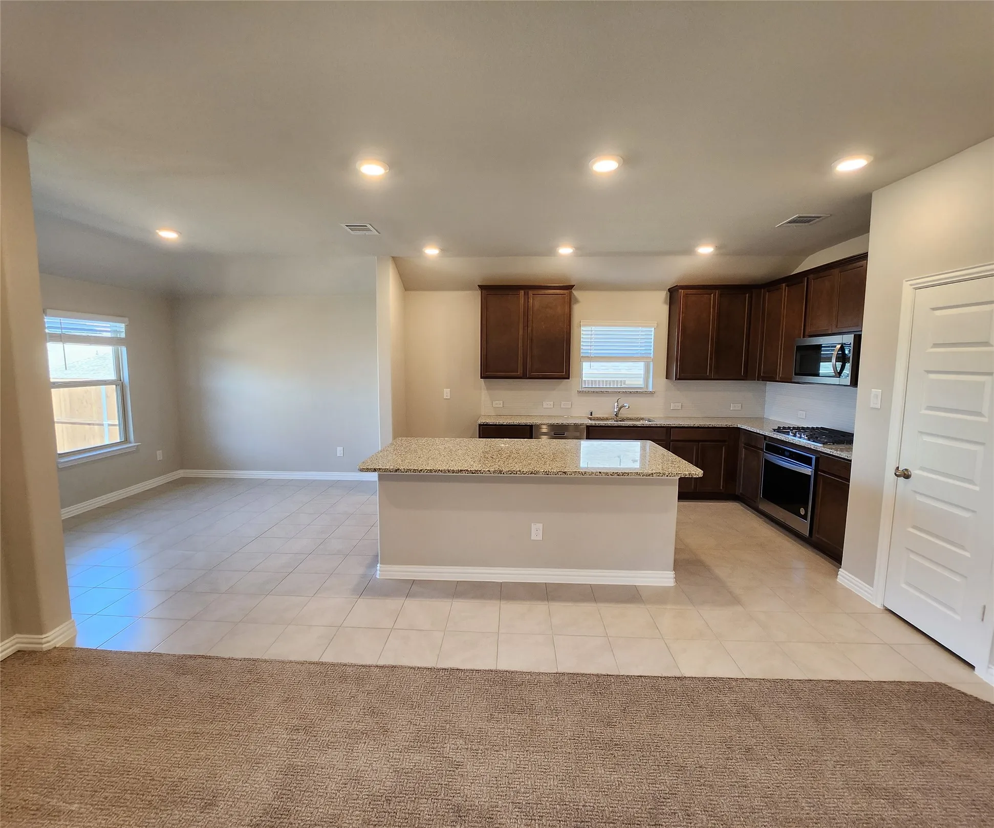 Open-concept kitchen with a granite island, dark wood cabinetry, and stainless steel appliances