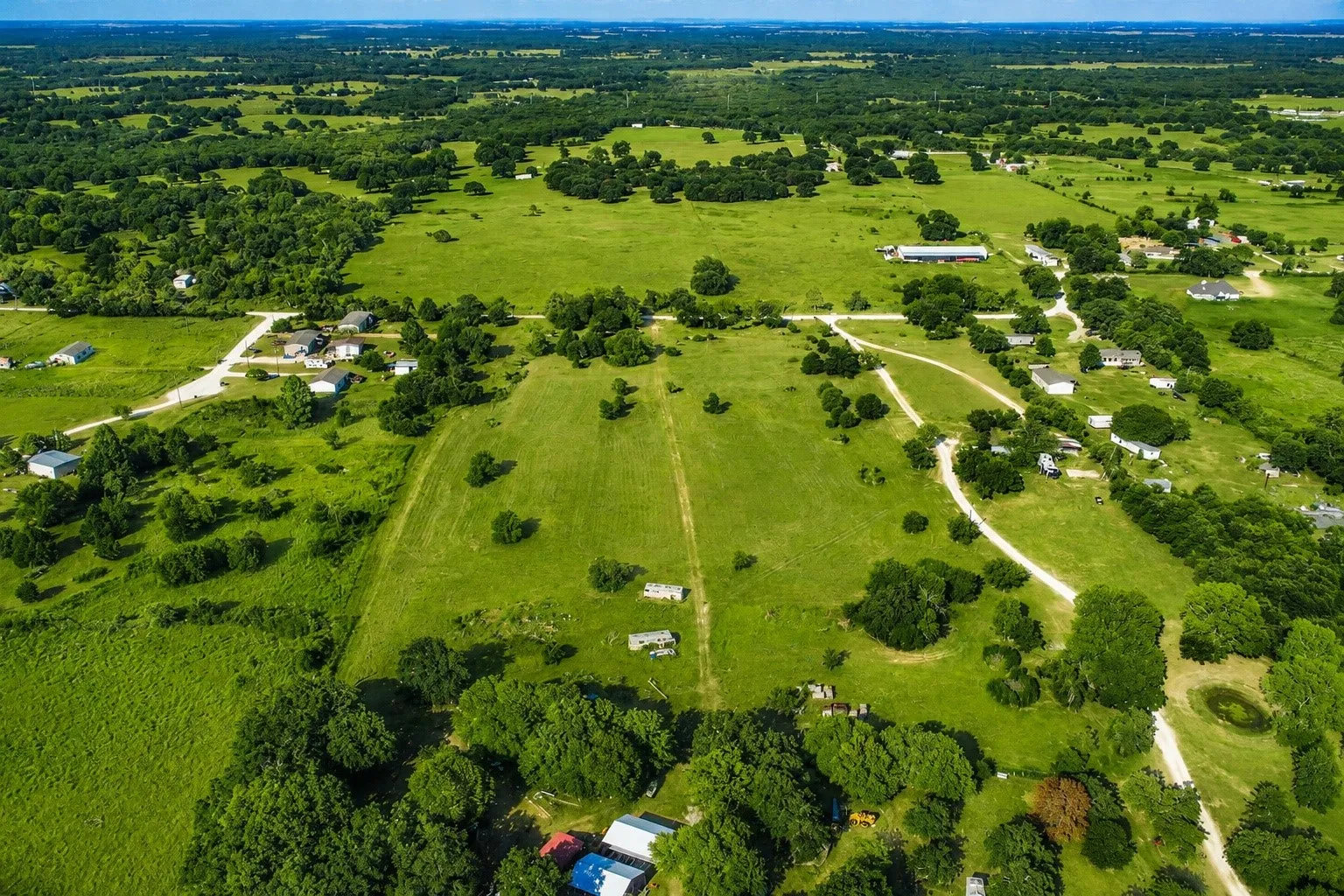 Expansive green landscape with scattered trees, a visible pond, and multiple residential structures