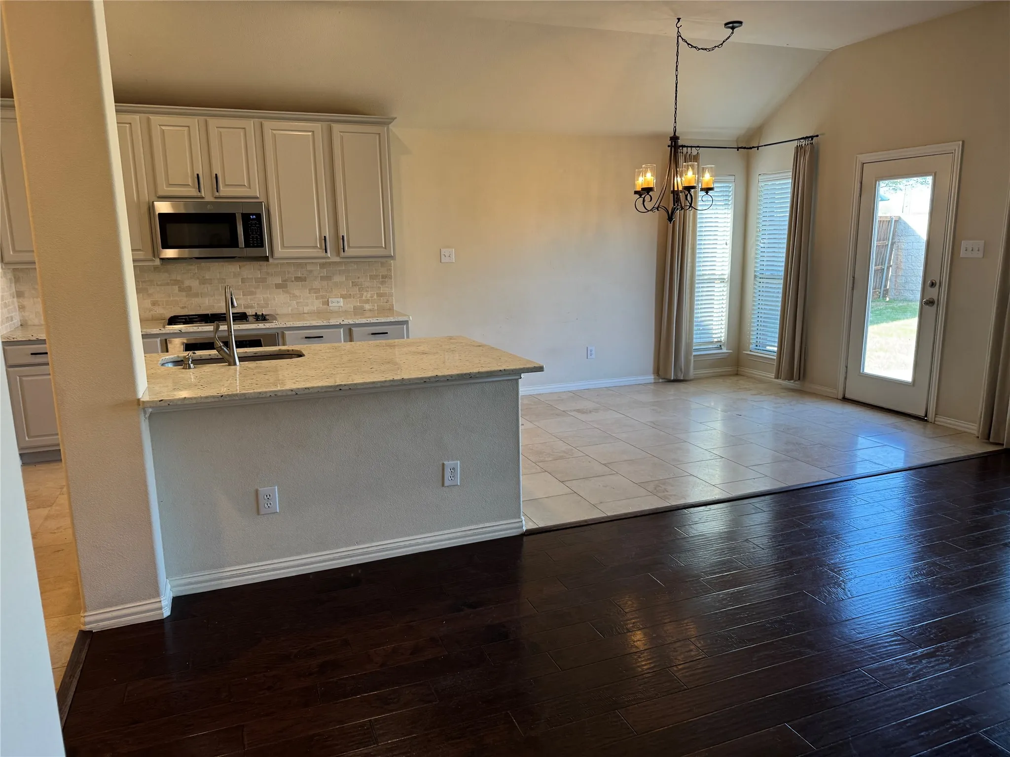 Kitchen featuring tasteful backsplash, an inviting chandelier, a sink, stainless steel microwave, and vaulted ceiling