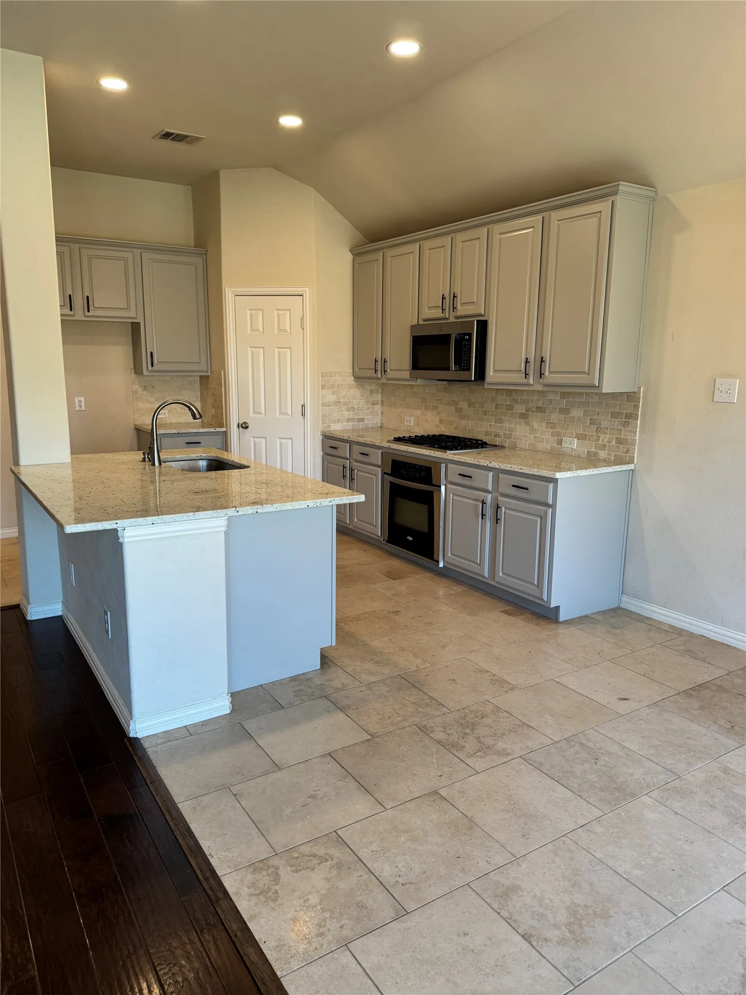Kitchen featuring a sink, vaulted ceiling, light stone countertops, gray cabinets, and stainless steel appliances