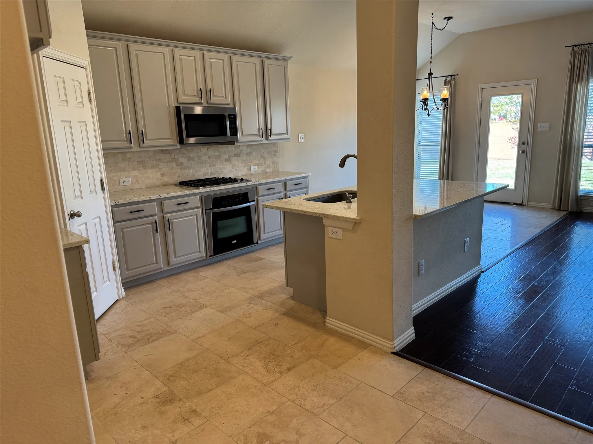 Kitchen with gray cabinets, appliances with stainless steel finishes, light stone counters, a sink, and decorative backsplash