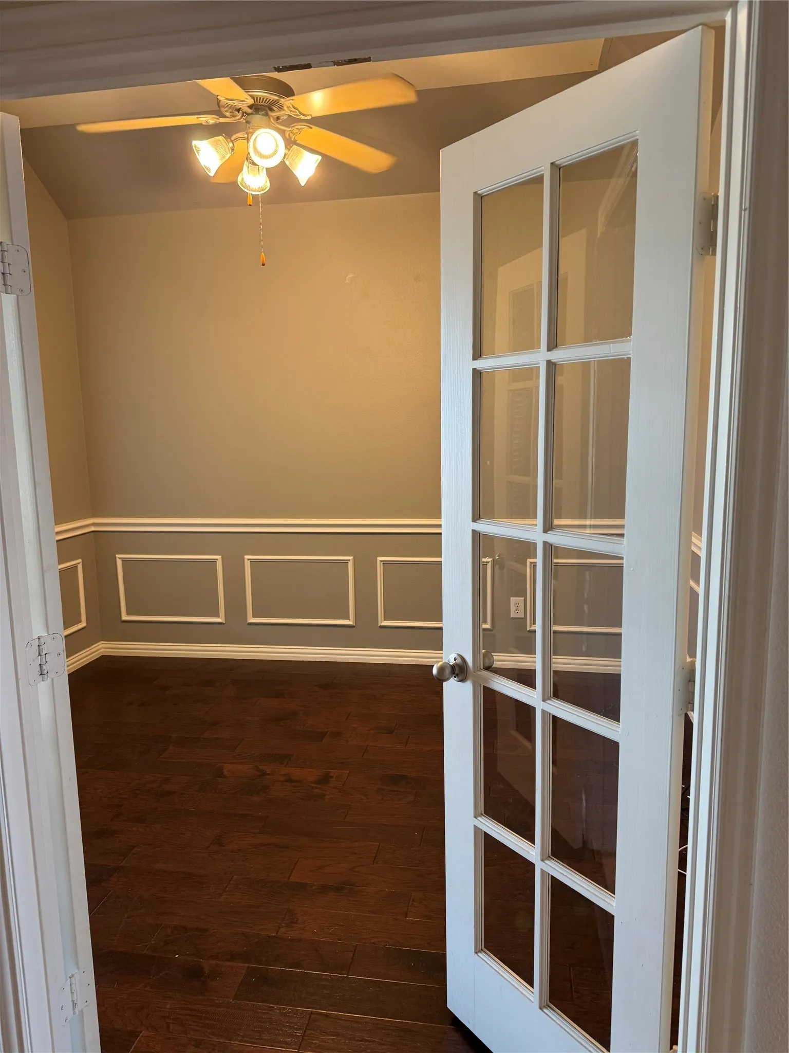 Office featuring a decorative wall, a ceiling fan, wainscoting, and dark wood finished floors