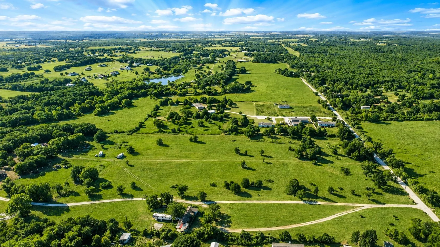 Expansive green acreage featuring scattered trees, a visible pond, and multiple structures