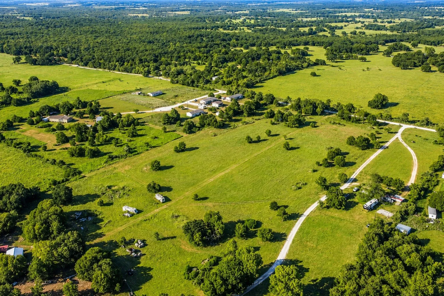 Sprawling rural property featuring expansive manicured pastures, mature tree clusters throughout, and a winding paved driveway