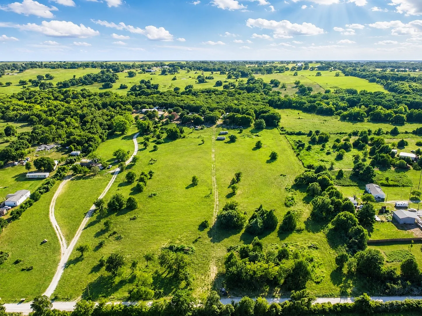 Expansive green landscape with scattered trees, multiple structures, and unpaved pathways