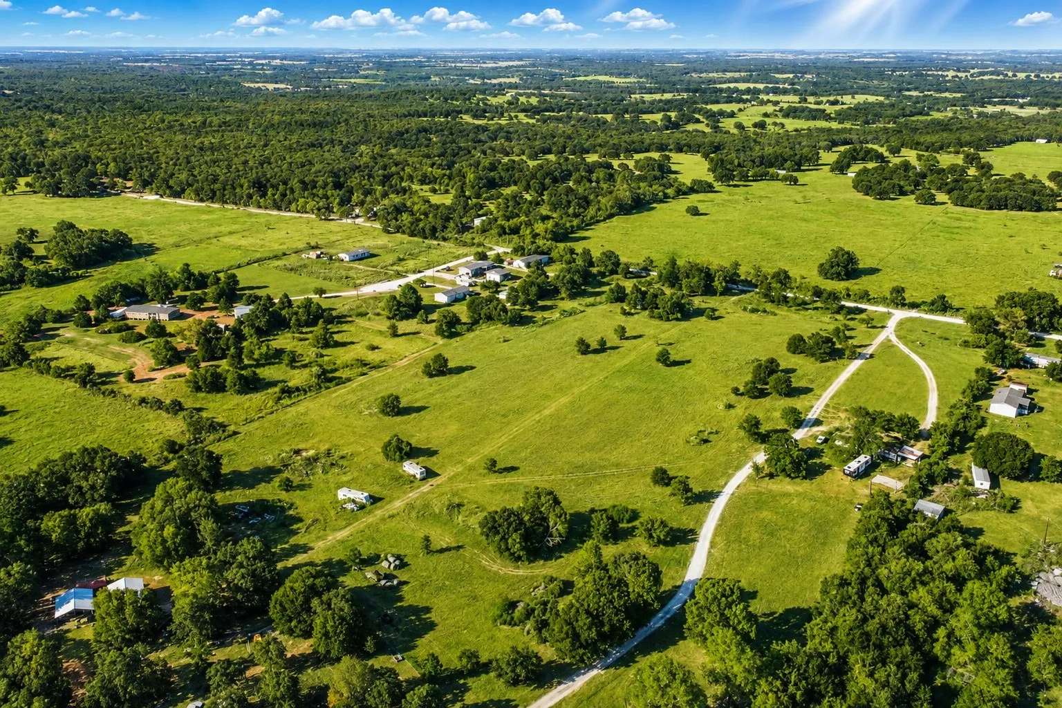 Expansive rural landscape featuring green pastures, scattered mature trees, and a distant forested horizon