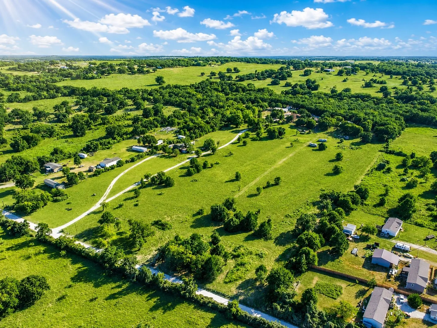 Expansive green landscape with scattered trees, multiple structures, and a network of unpaved roads