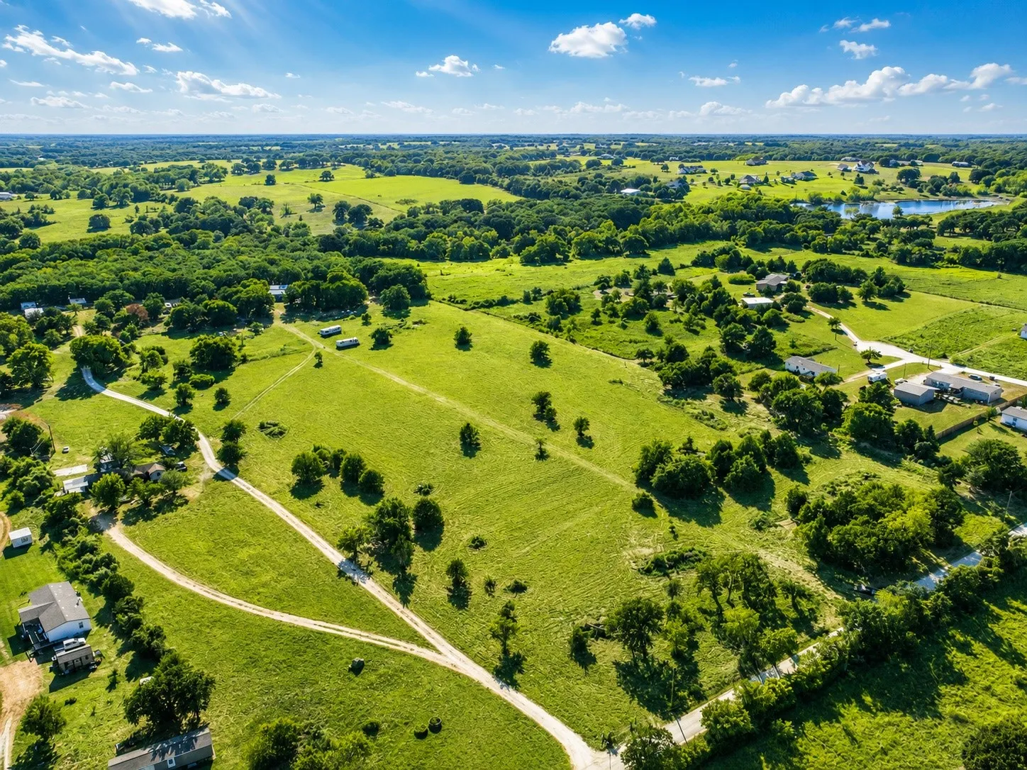 Expansive green acreage with scattered trees and a visible pond