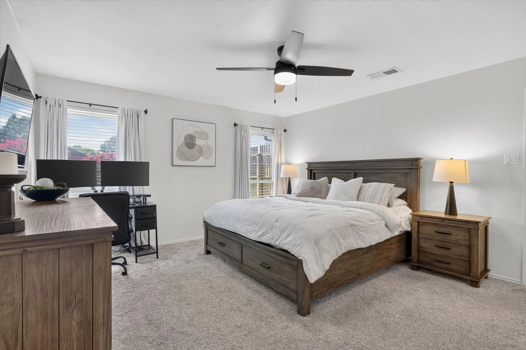 Spacious room featuring light-colored carpeting, multiple windows with blinds, and a ceiling fan with integrated lighting