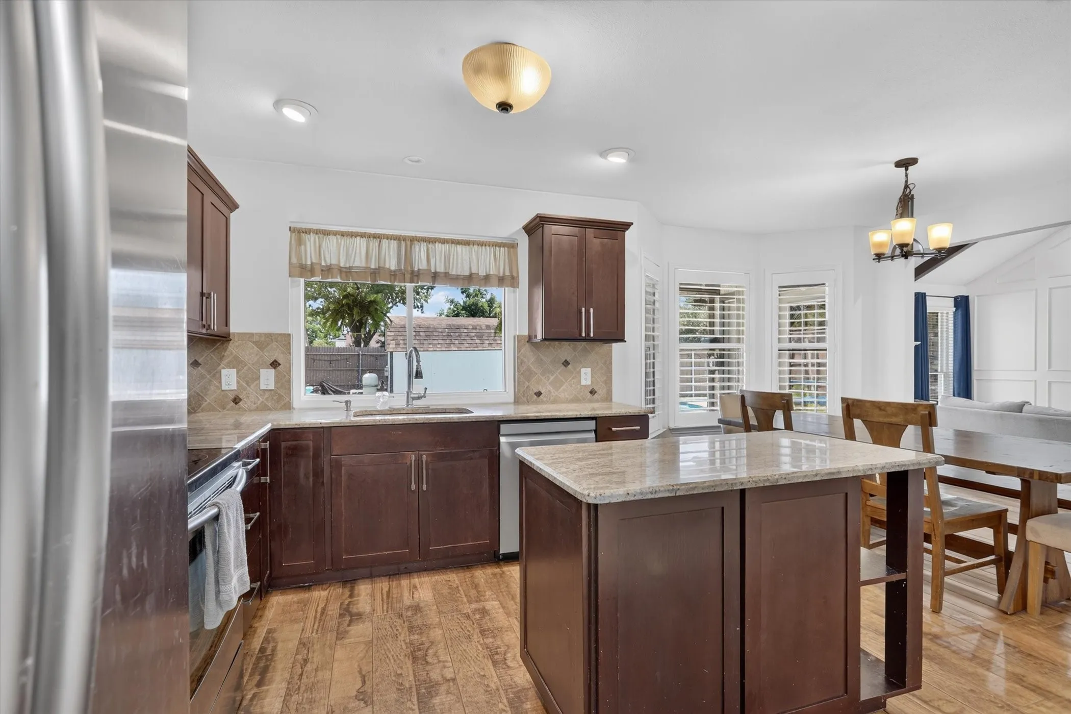 Kitchen featuring wood-finish tile flooring, dark wood cabinetry, light-toned countertops, and a tiled backsplash