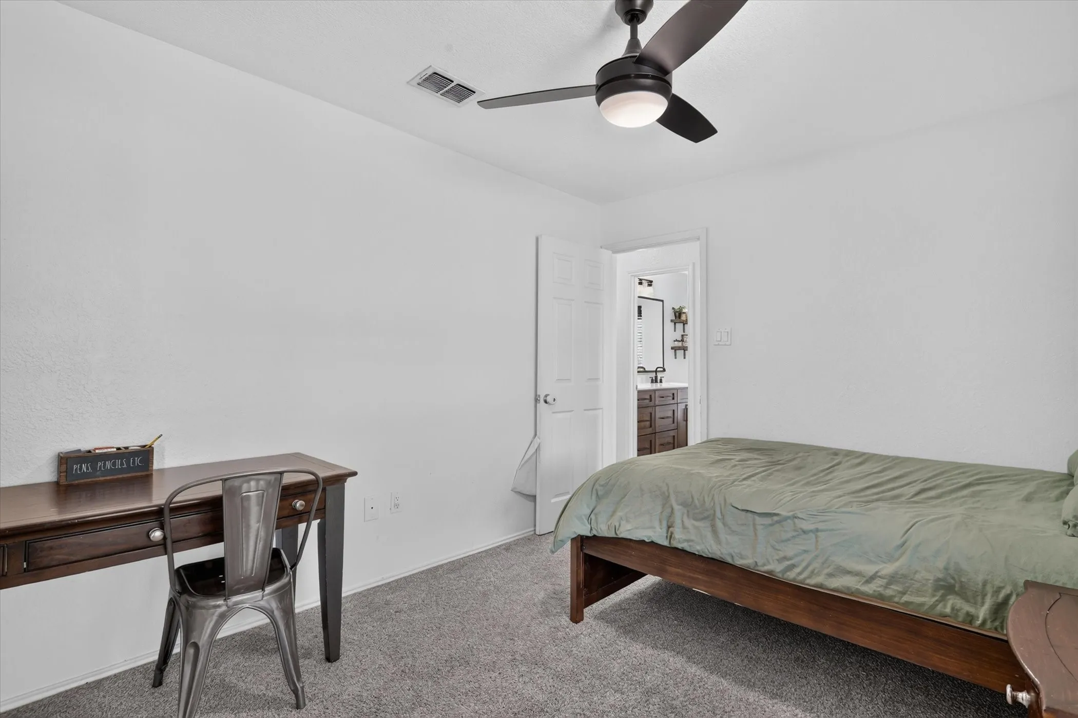 Recessed lighting, ceiling fan, carpet flooring, and a doorway opening to a bathroom with a dark wood-finish vanity