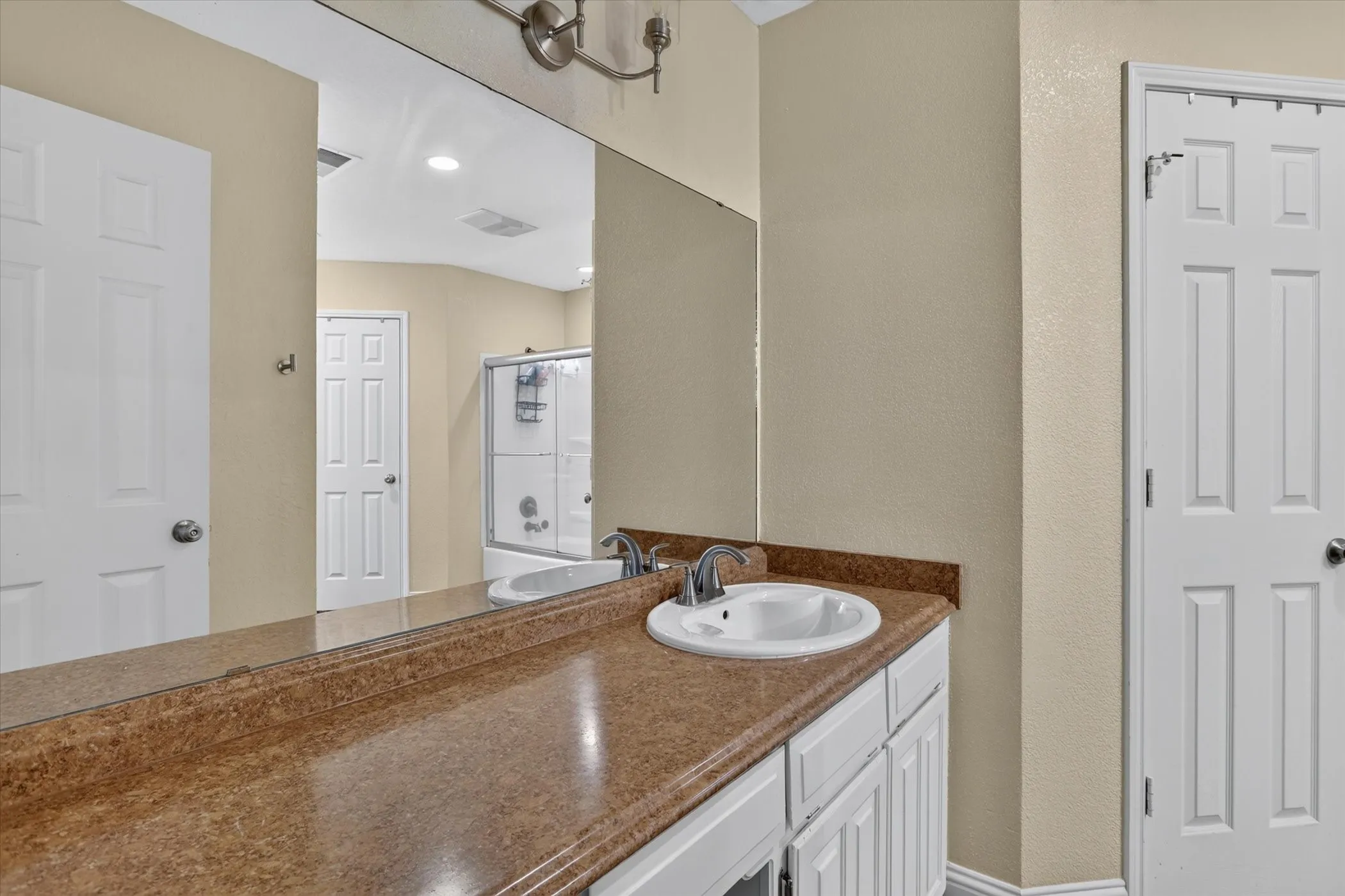 Dual-paneled interior doors, a large vanity mirror, and a white integrated sink with a chrome faucet