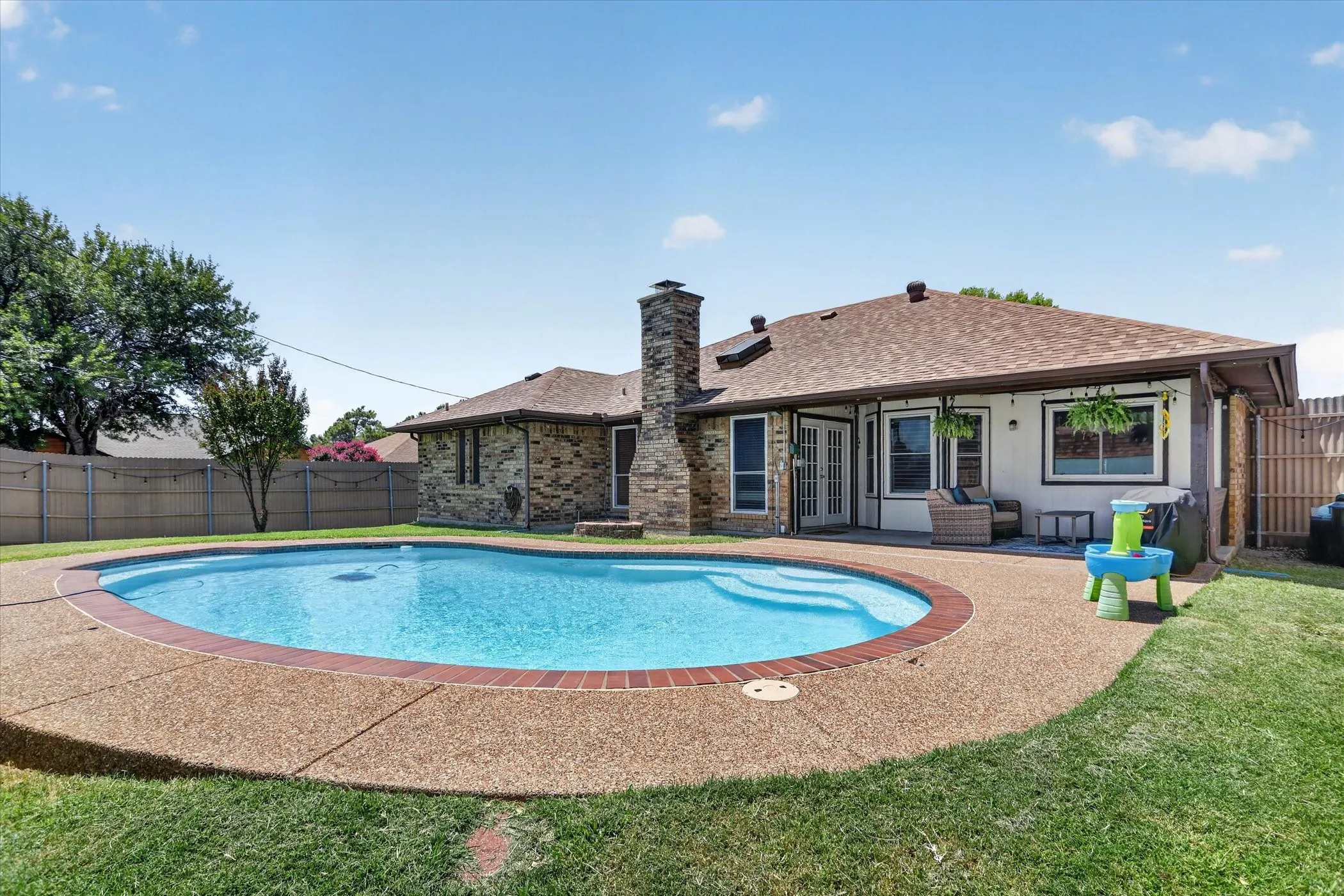 In-ground swimming pool with an aggregate concrete deck, brick-clad exterior, and a built-in stone chimney