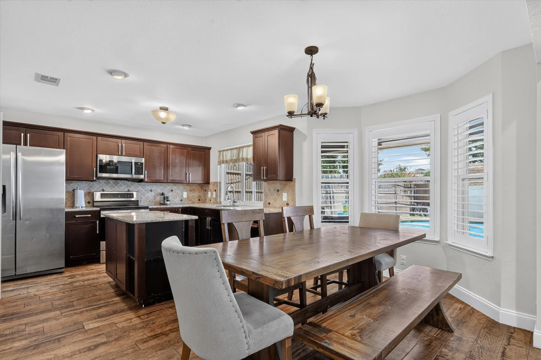 Kitchen featuring wood-finish tile flooring, dark wood cabinetry, stainless steel appliances, and a tiled backsplash