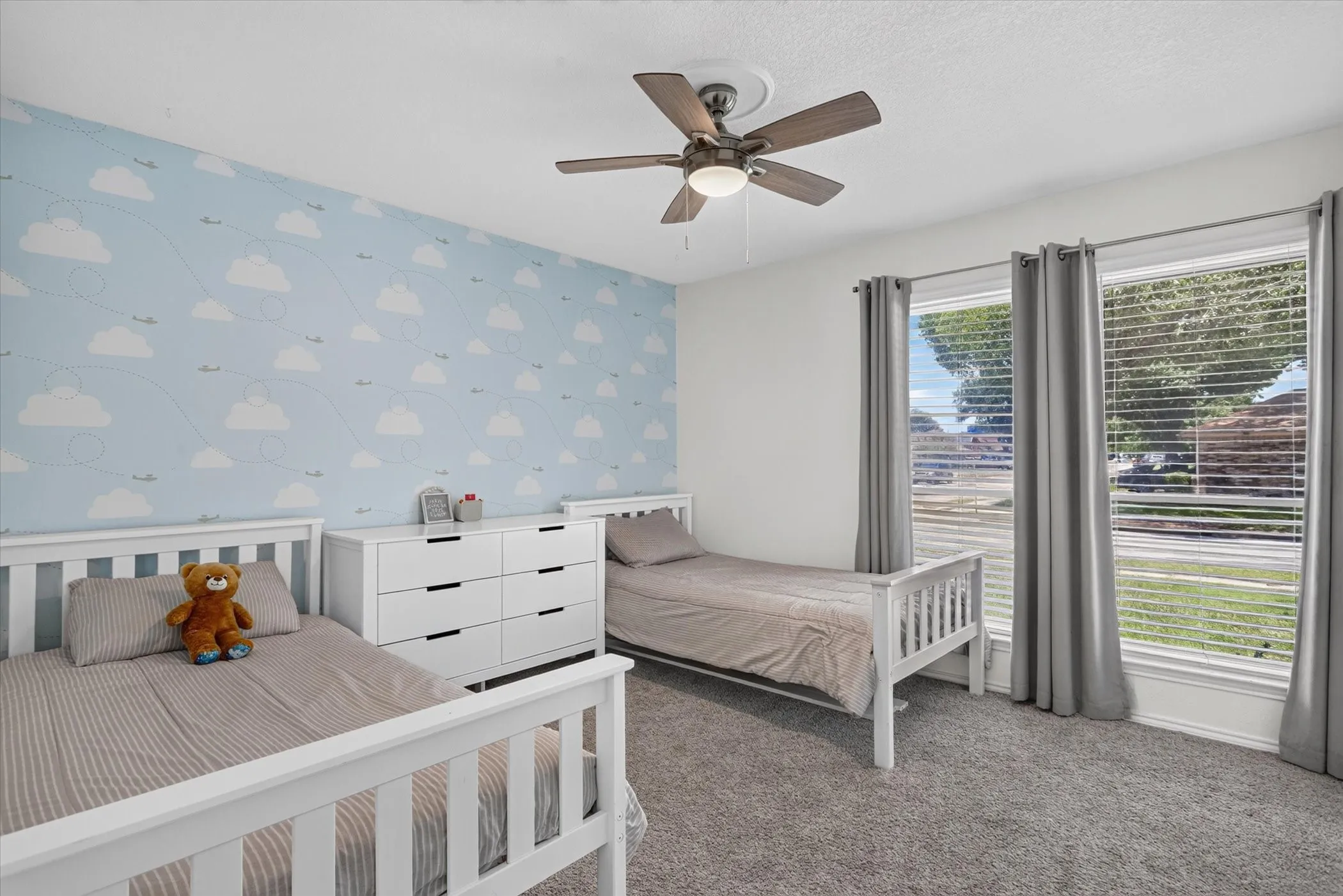Soft carpeting, two large windows, a ceiling fan with integrated lighting, and a feature wall