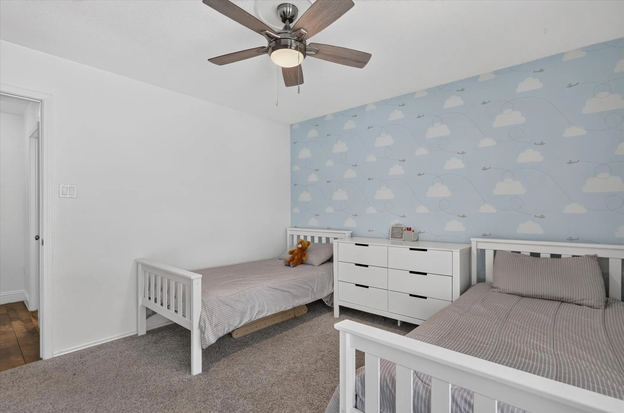 Ceiling fan with light fixture, carpeted flooring, and a decorative accent wall